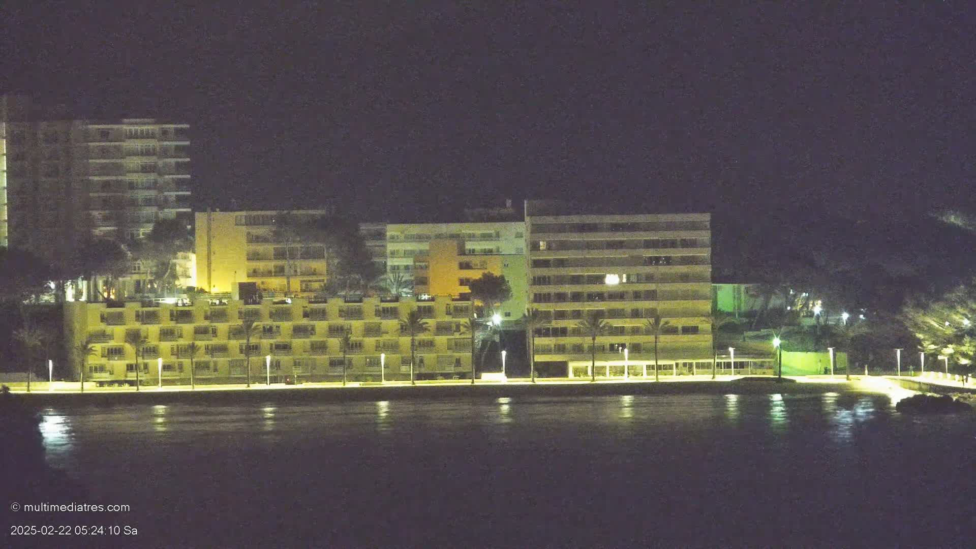 A row of illuminated buildings sits along a dark waterfront at night.