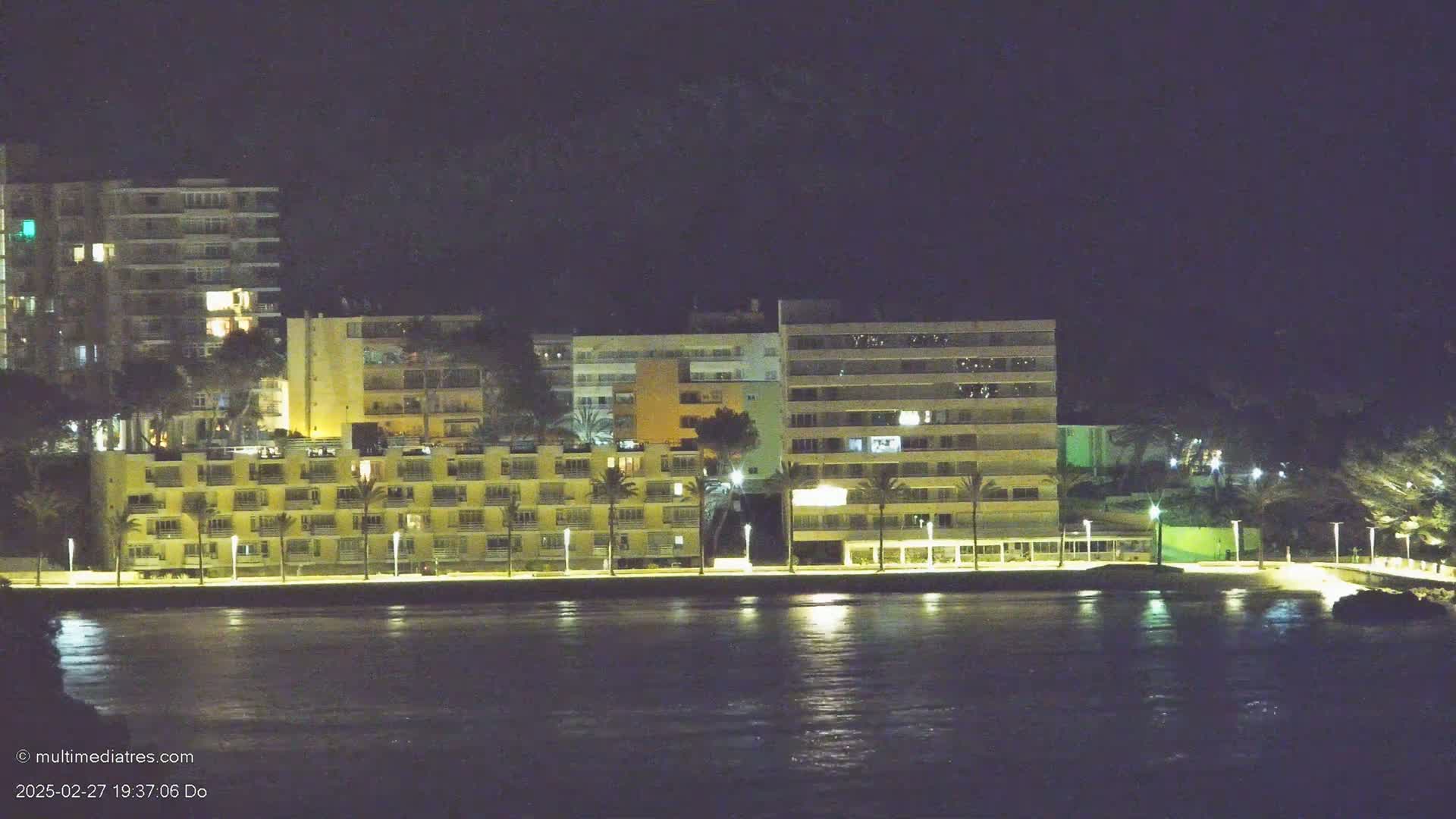 A row of illuminated apartment buildings lines a dark waterfront at night.