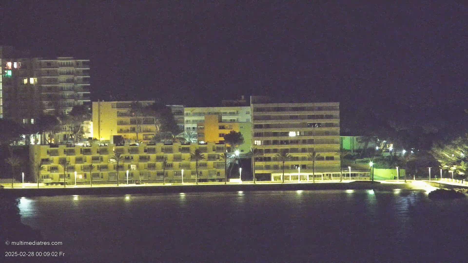 A row of illuminated buildings lines a dark waterfront at night.