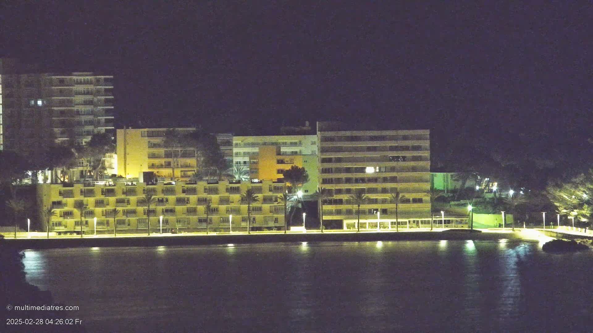 Illuminated multi-story buildings line a waterfront at night.