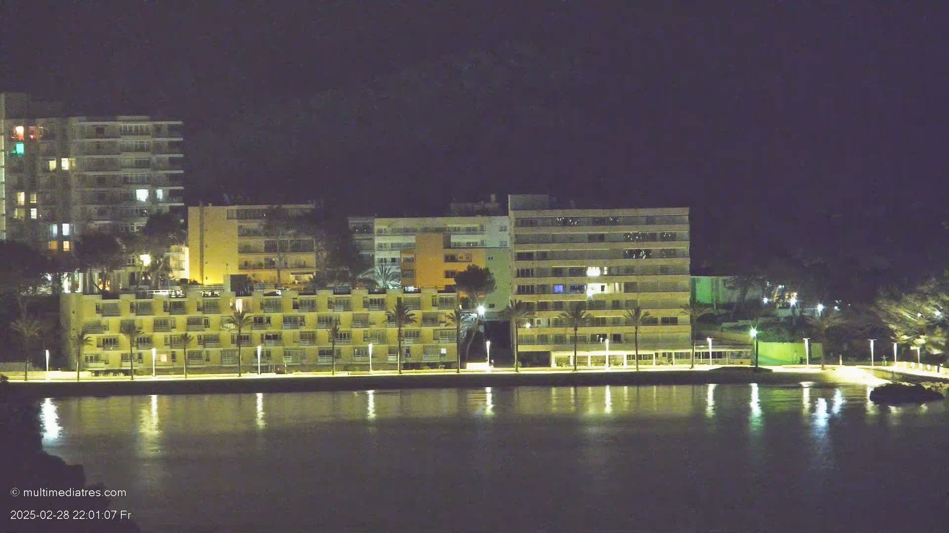 A row of illuminated buildings lines a calm, dark waterfront at night.