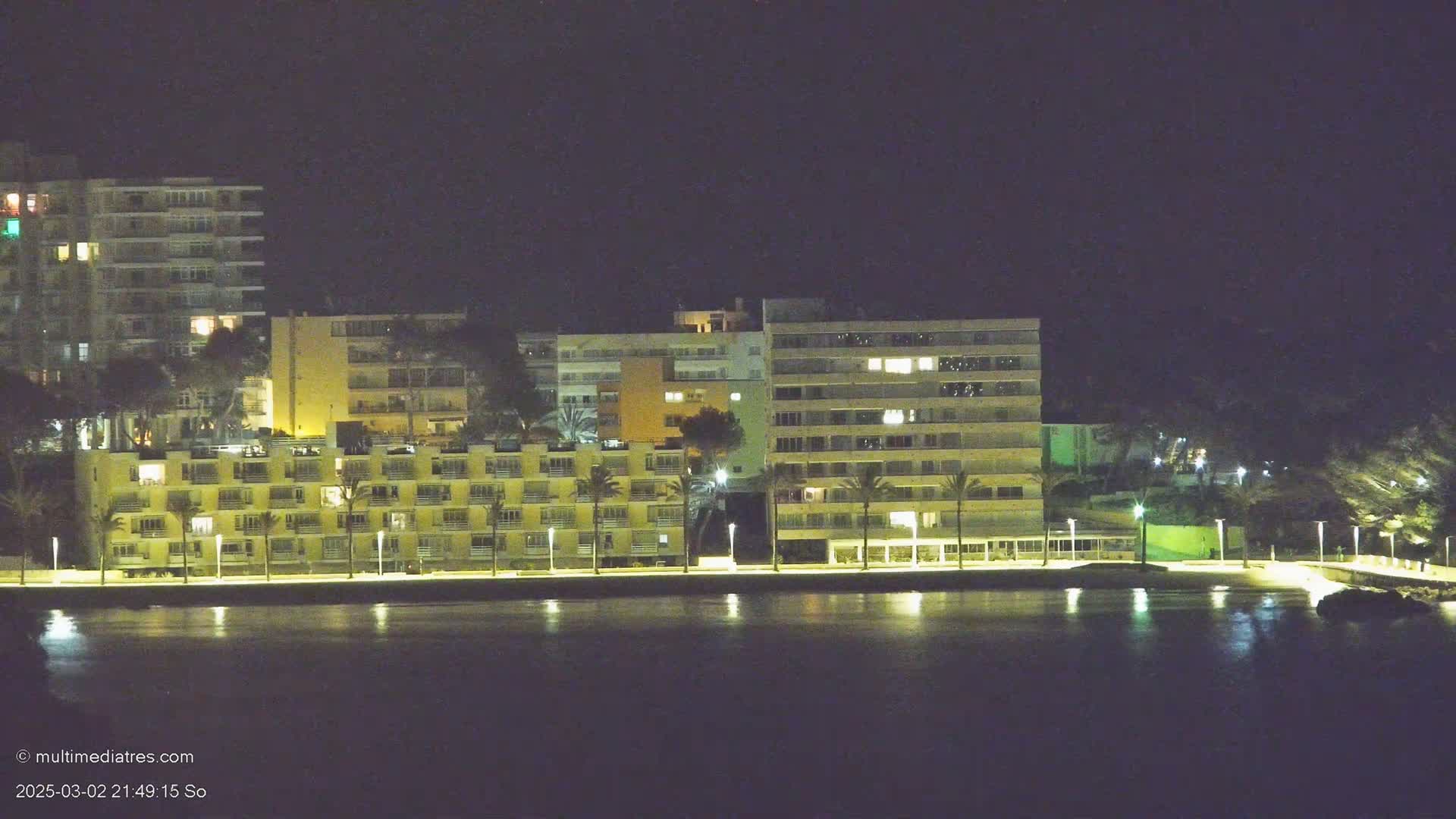 Illuminated apartment buildings line a calm waterfront at night.