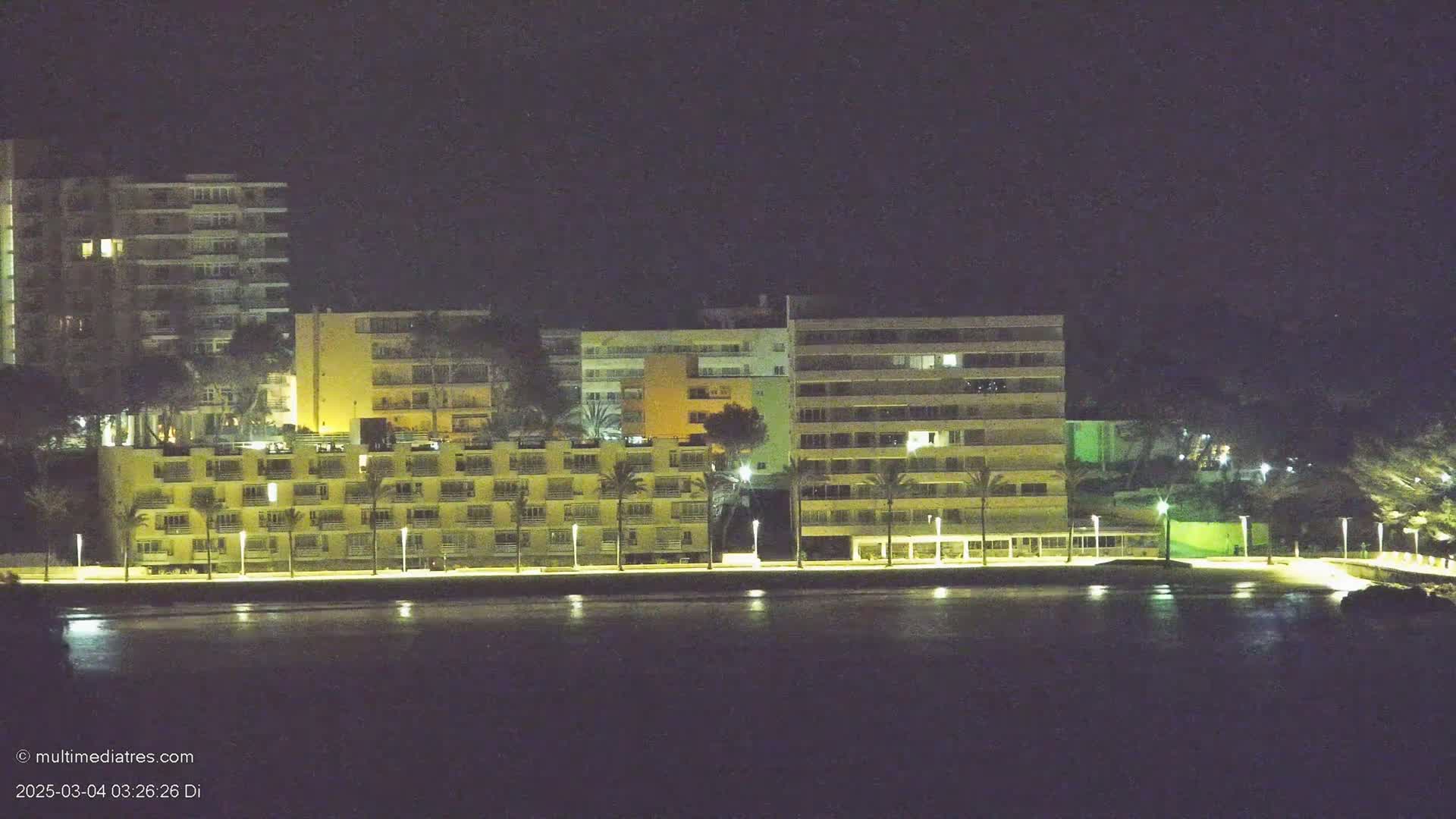 Illuminated multi-story buildings line a waterfront at night.