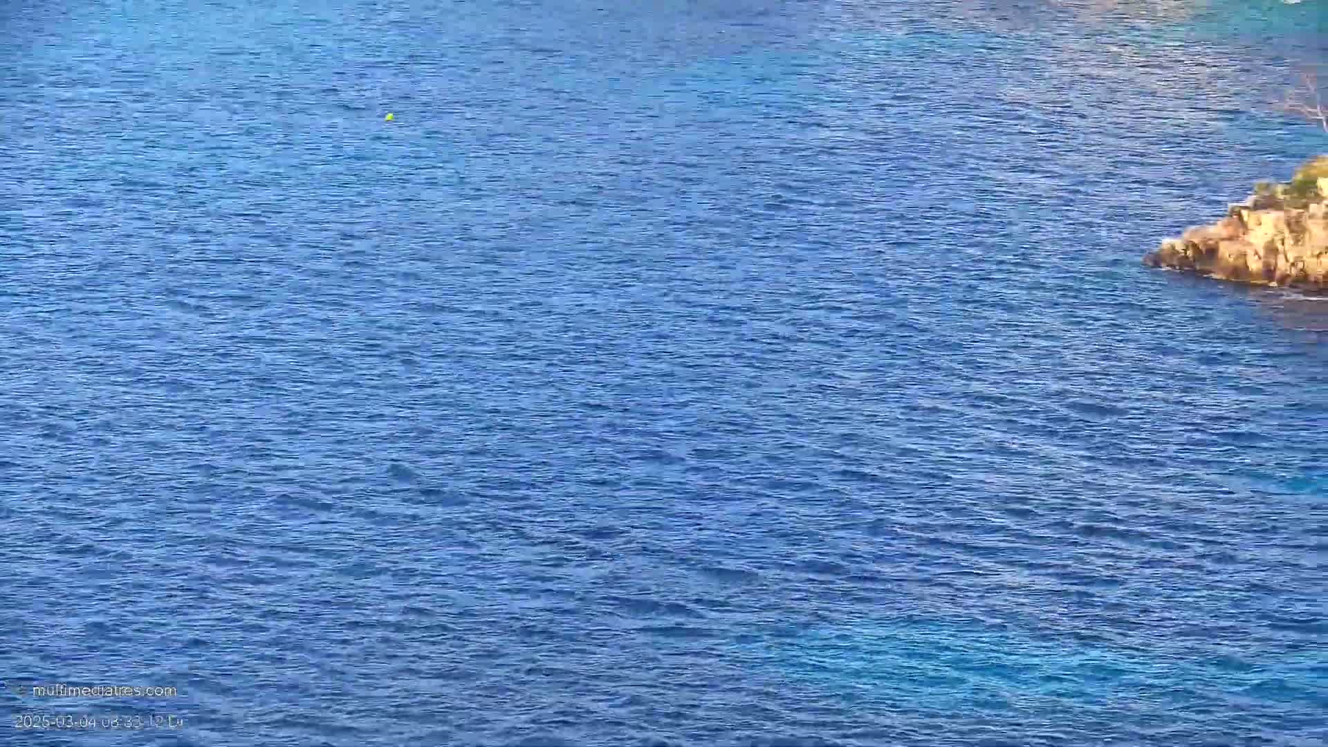 A rocky outcrop juts into a calm, deep blue sea.