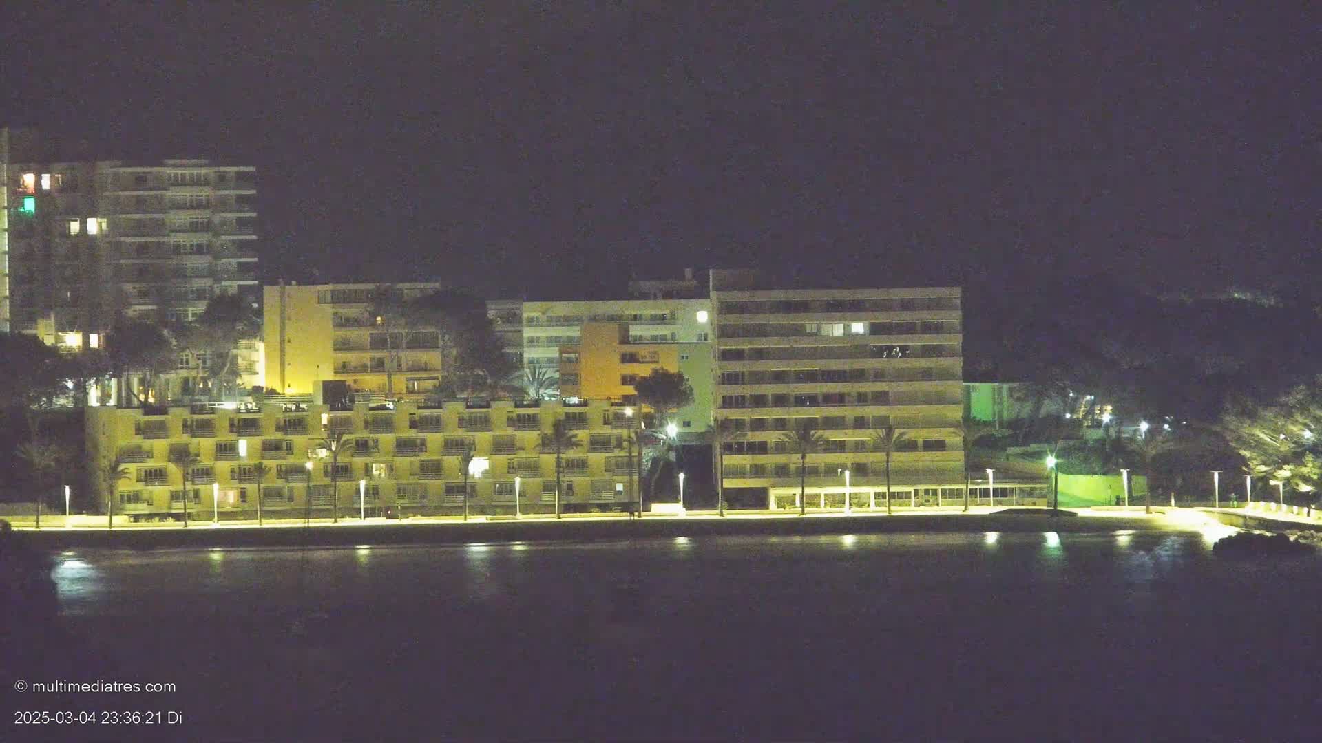 Several illuminated multi-story buildings line a dark waterfront at night.