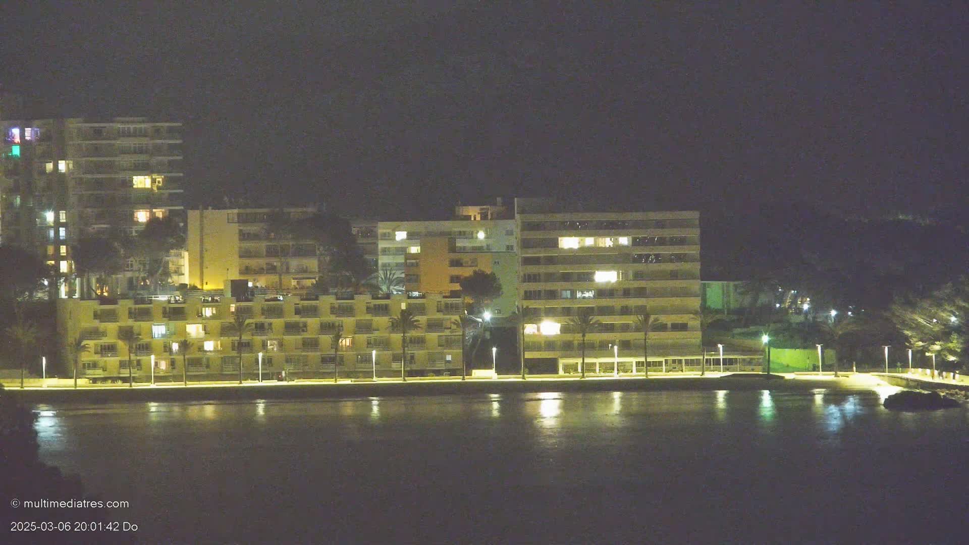 A row of illuminated buildings lines a calm body of water at night.
