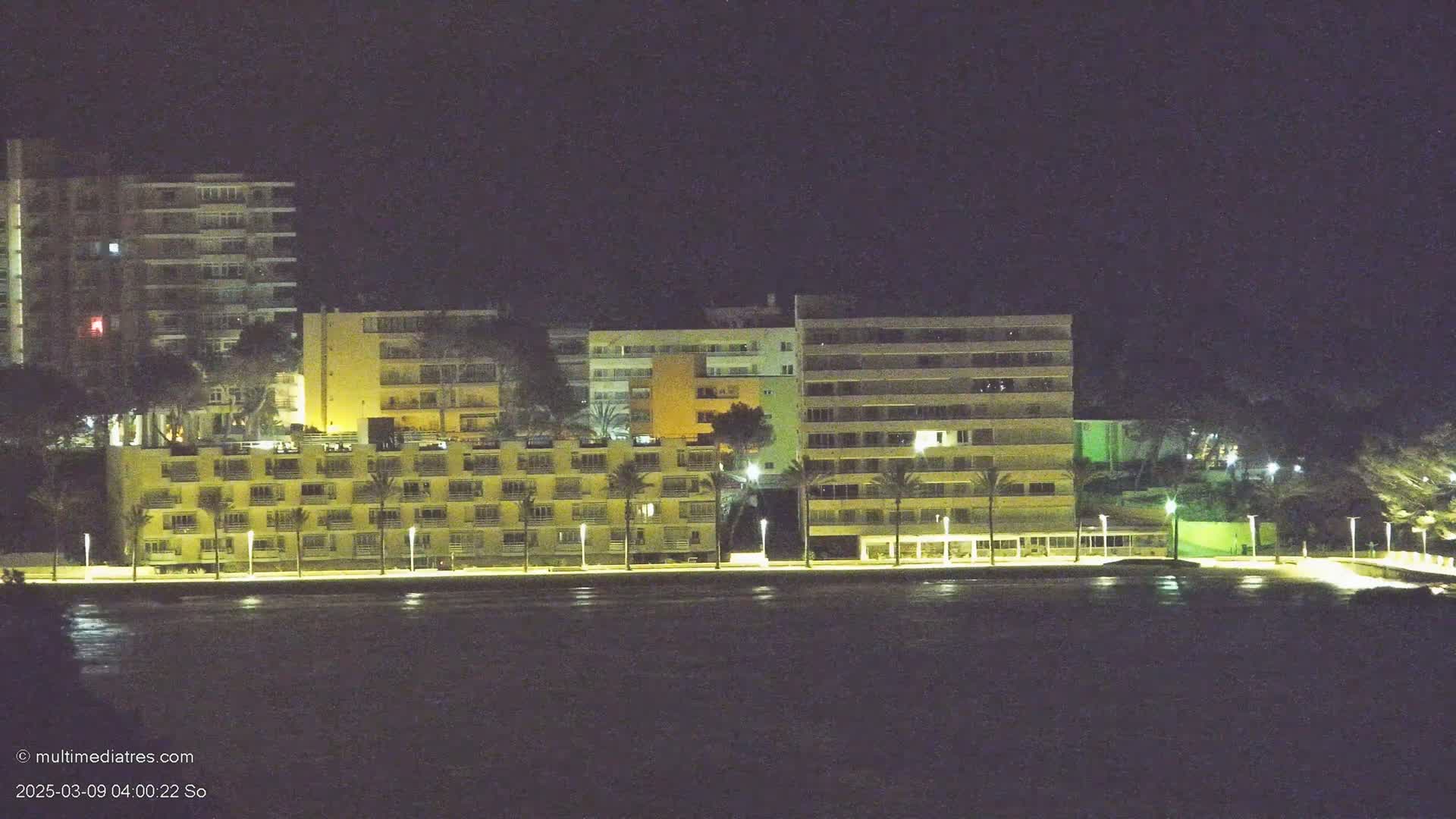 Illuminated multi-story buildings line a dark waterfront at night.