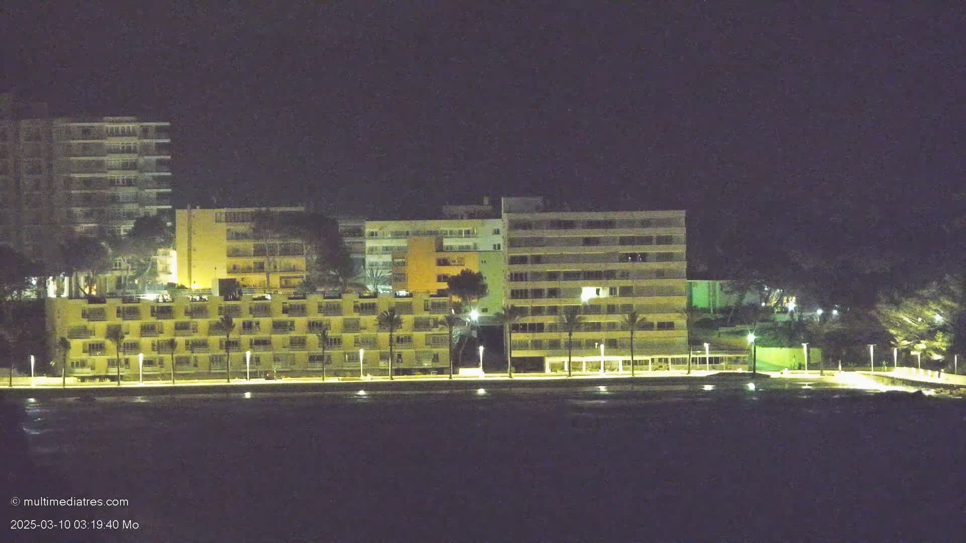 Several illuminated multi-story buildings line a waterfront at night.
