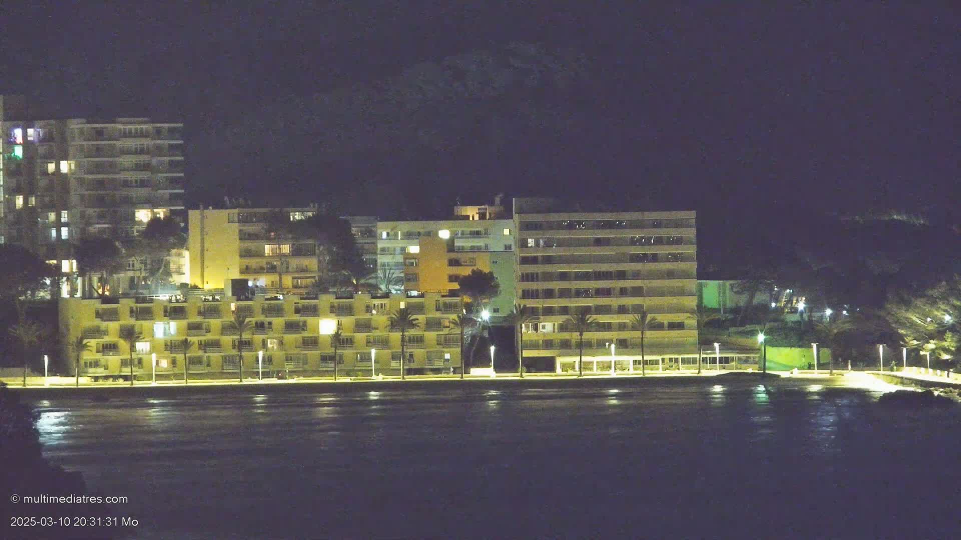 Illuminated apartment buildings line a dark waterfront at night.