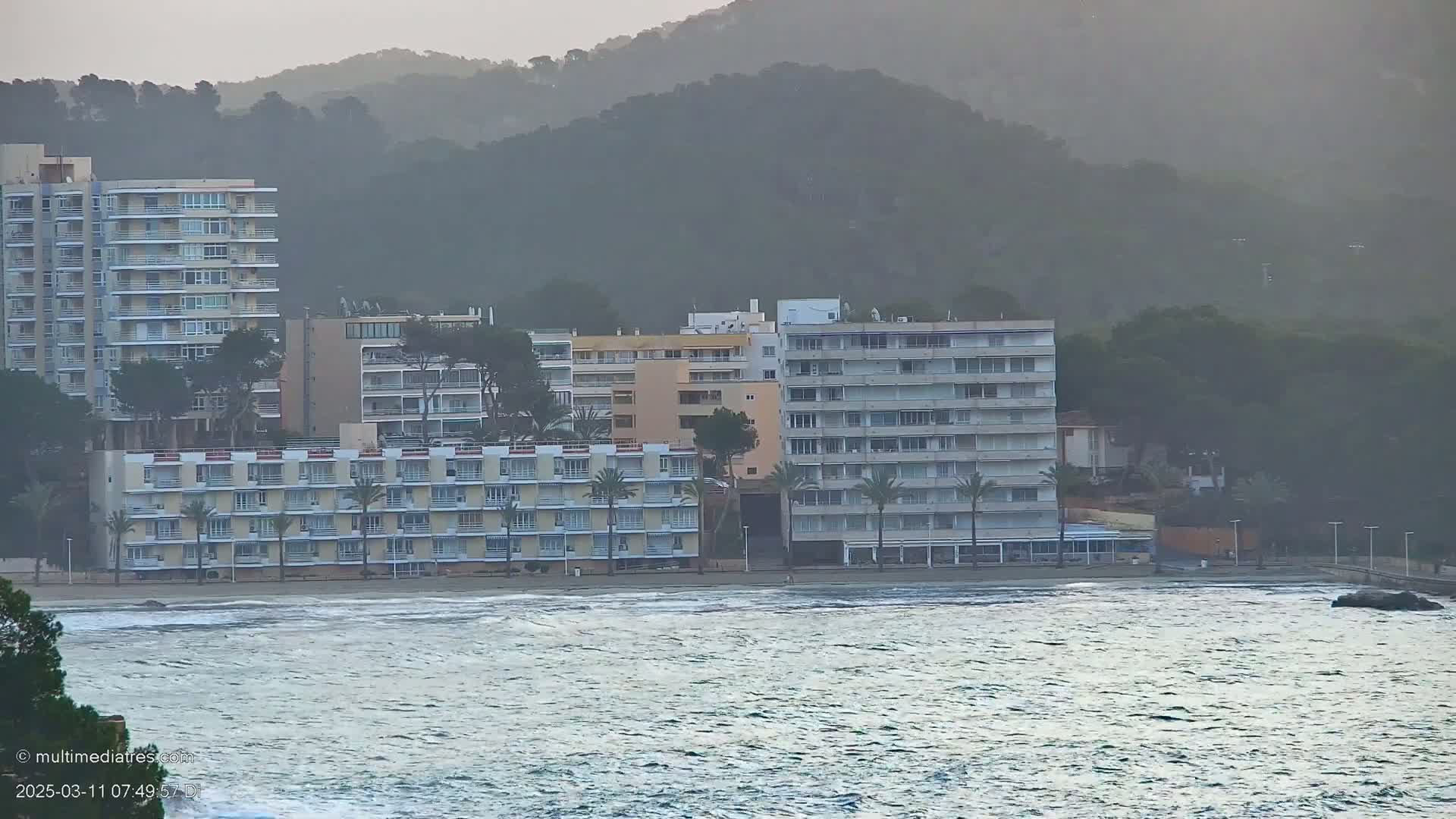 Several multi-story buildings line a beach with a somewhat choppy ocean under a hazy sky.