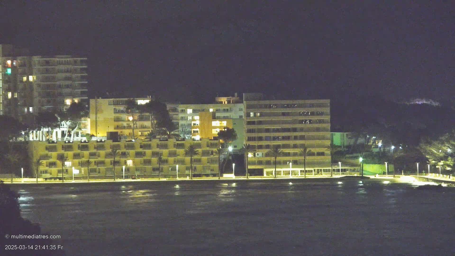 A line of illuminated buildings sits beside a dark body of water at night.