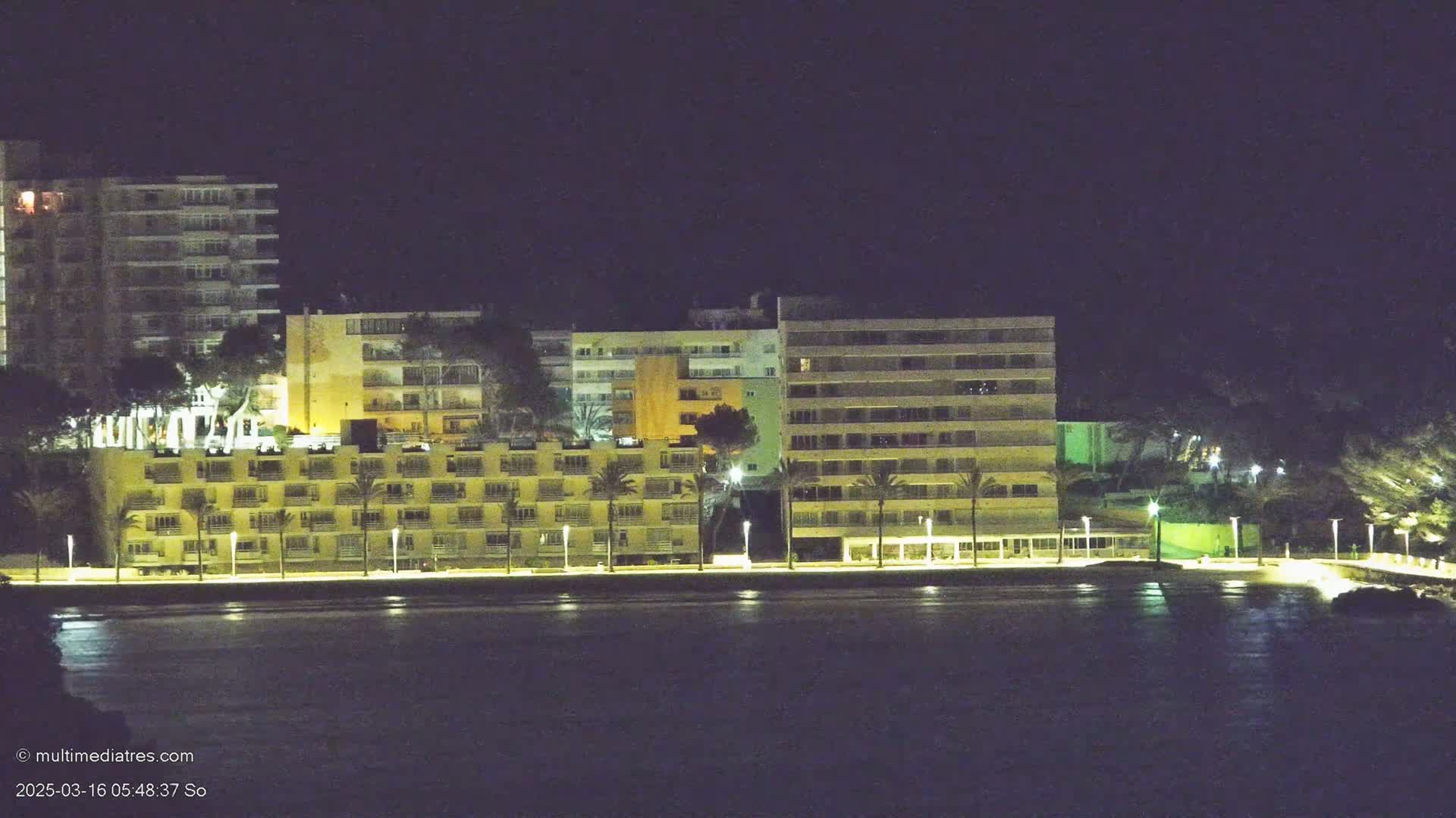 Illuminated apartment buildings line a waterfront at night.