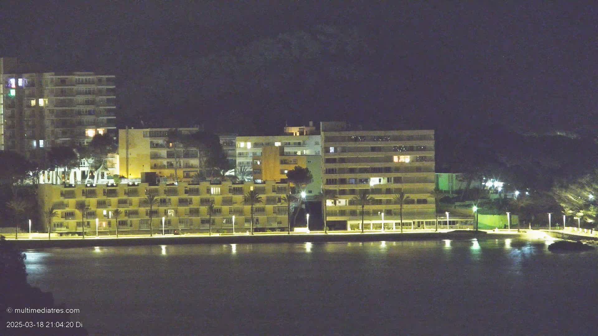 Several illuminated buildings line a waterfront at night.