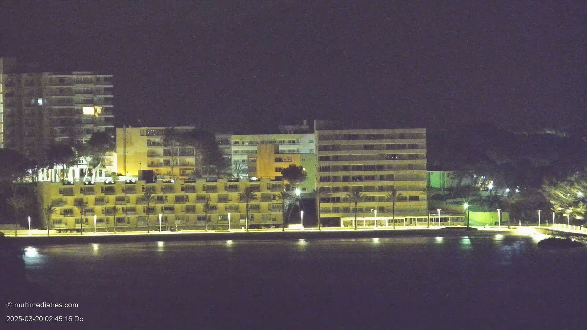A row of illuminated buildings stands along a dark waterfront at night.