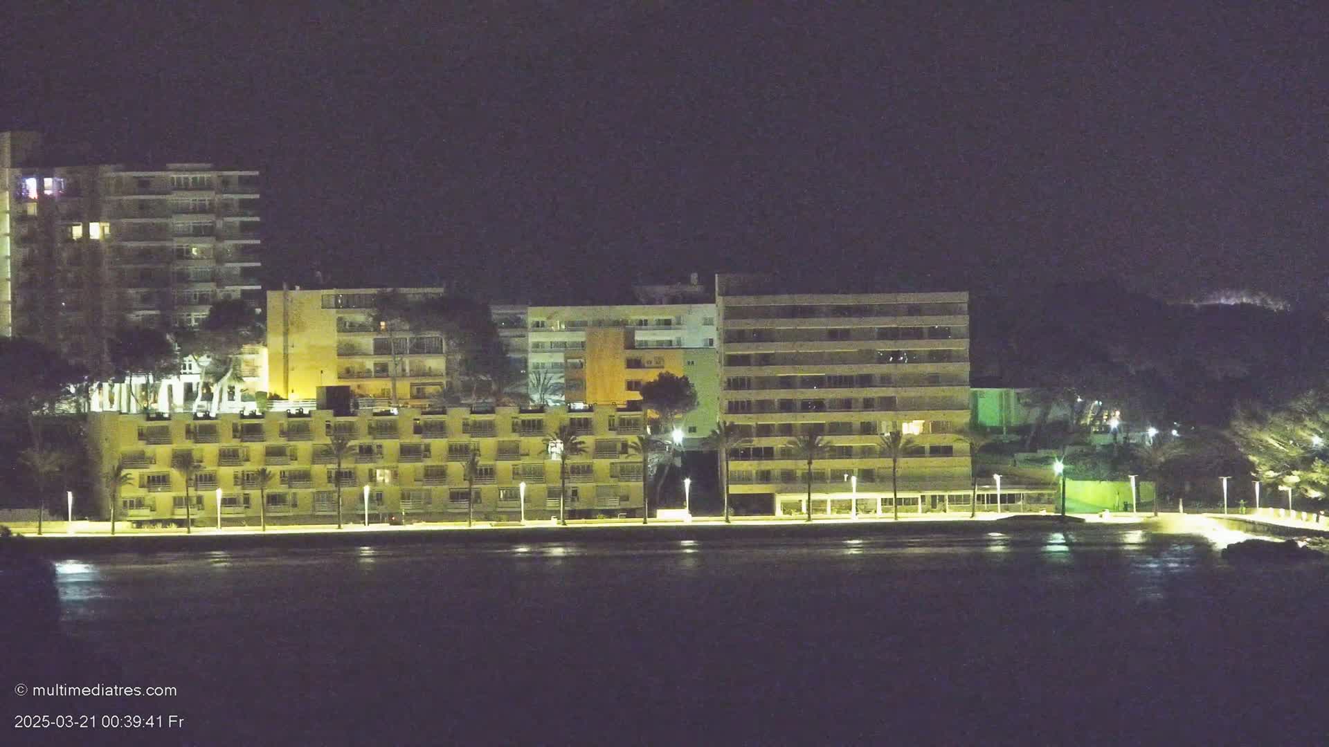 Illuminated multi-story buildings line a waterfront at night.