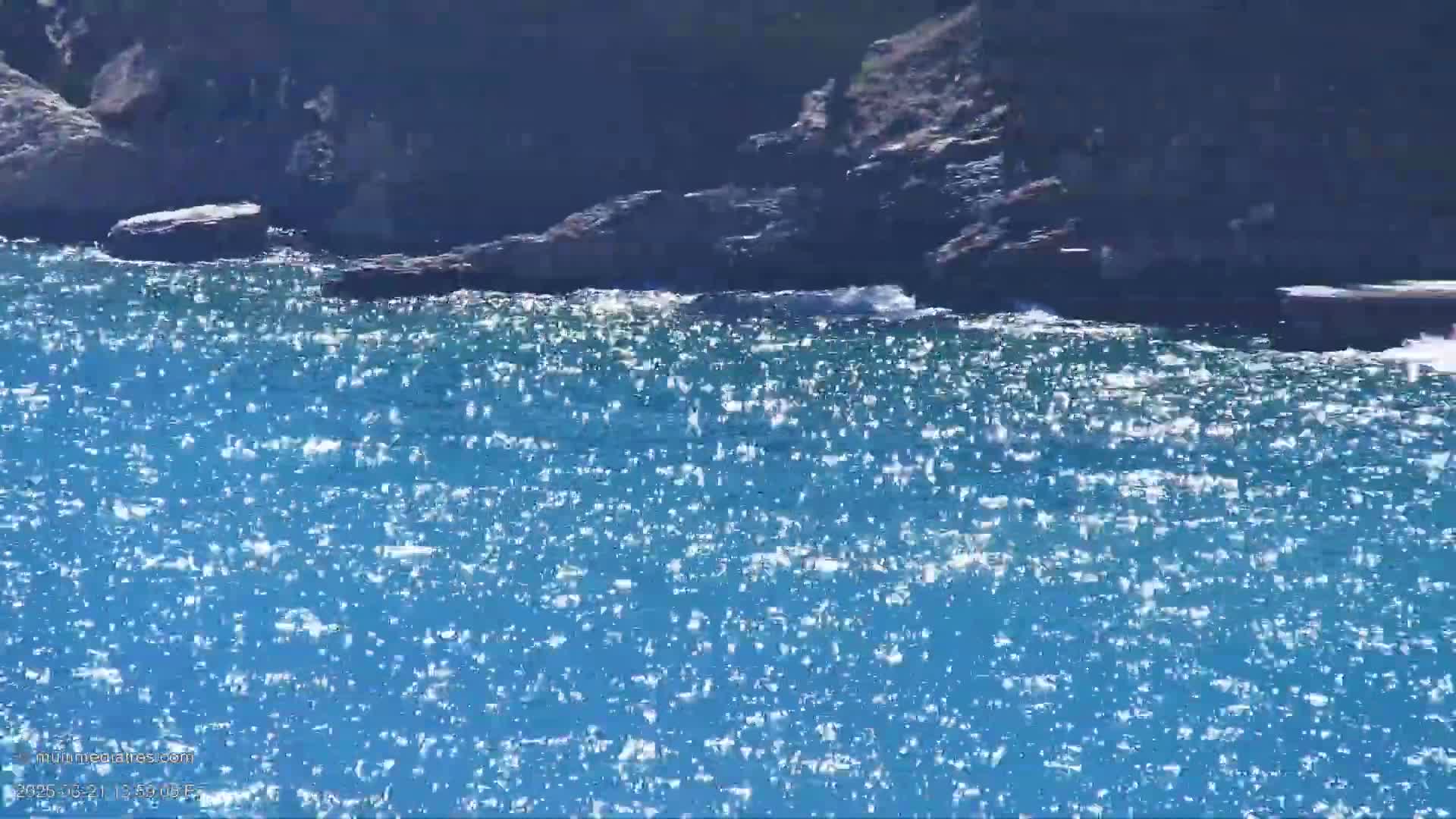 Sparkling blue water laps against dark rocks on a sunny day.