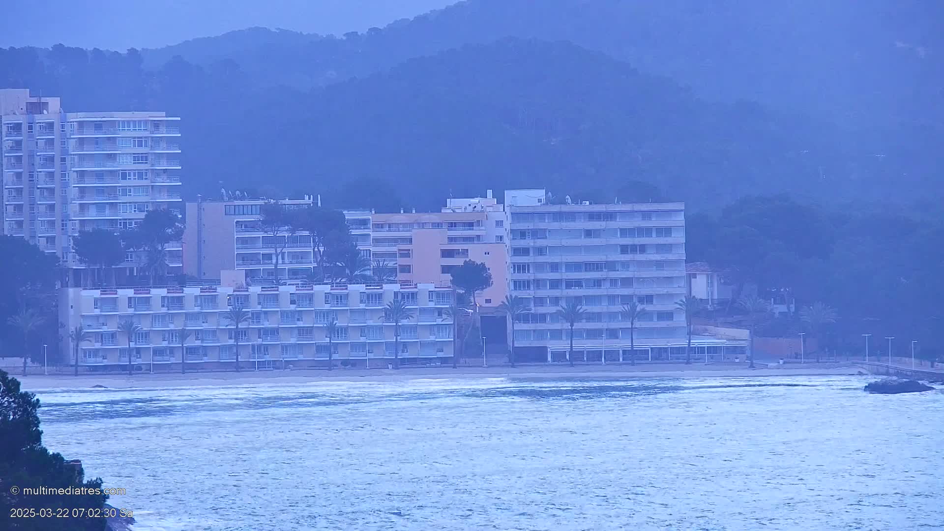A hazy, overcast day shows several multi-story buildings along a beach with choppy water.