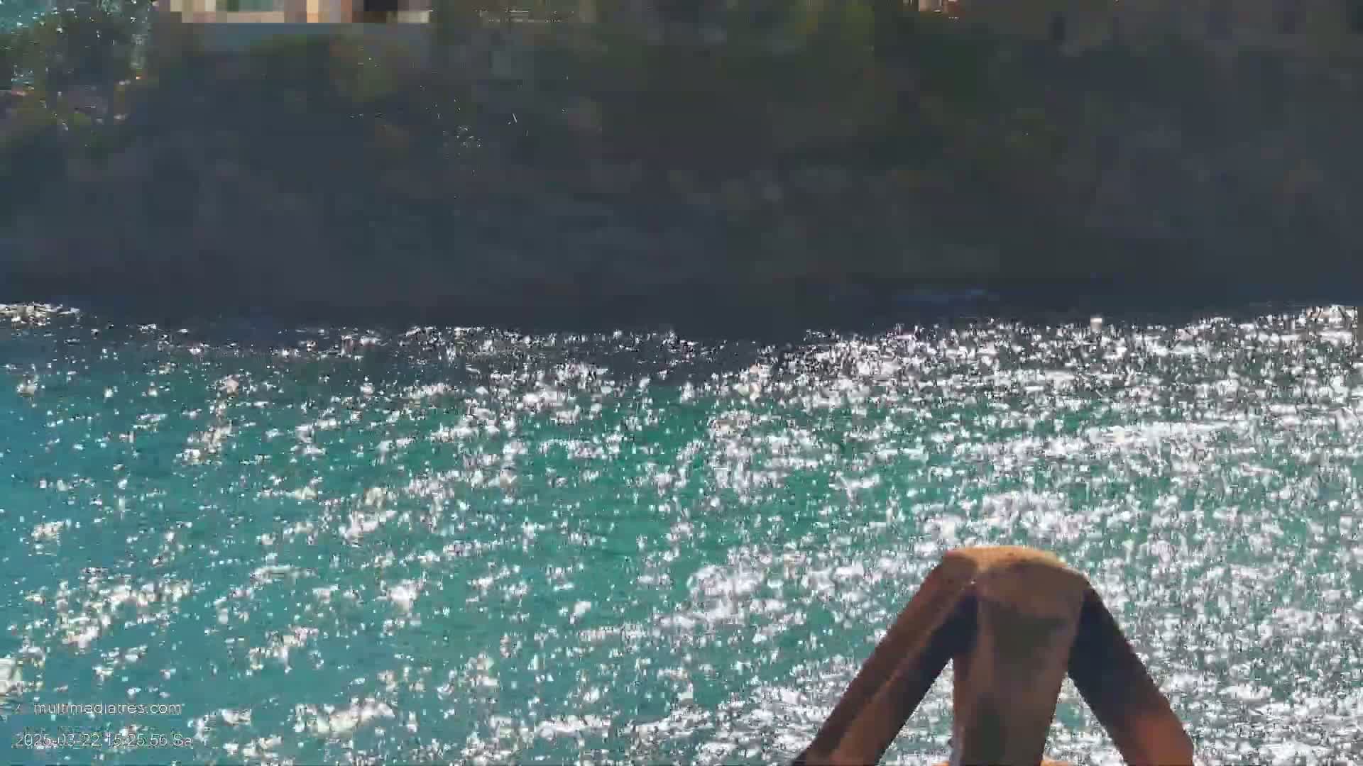 Sparkling teal water shimmers under a sunny sky near a dark, rocky shoreline.