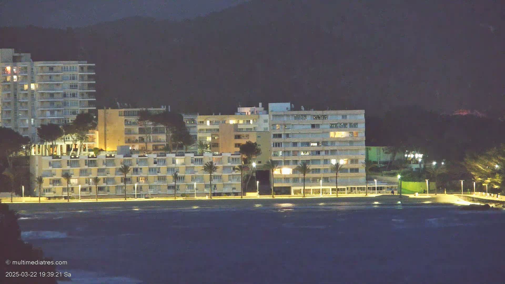 Illuminated apartment buildings line a beach at night under a dark sky.