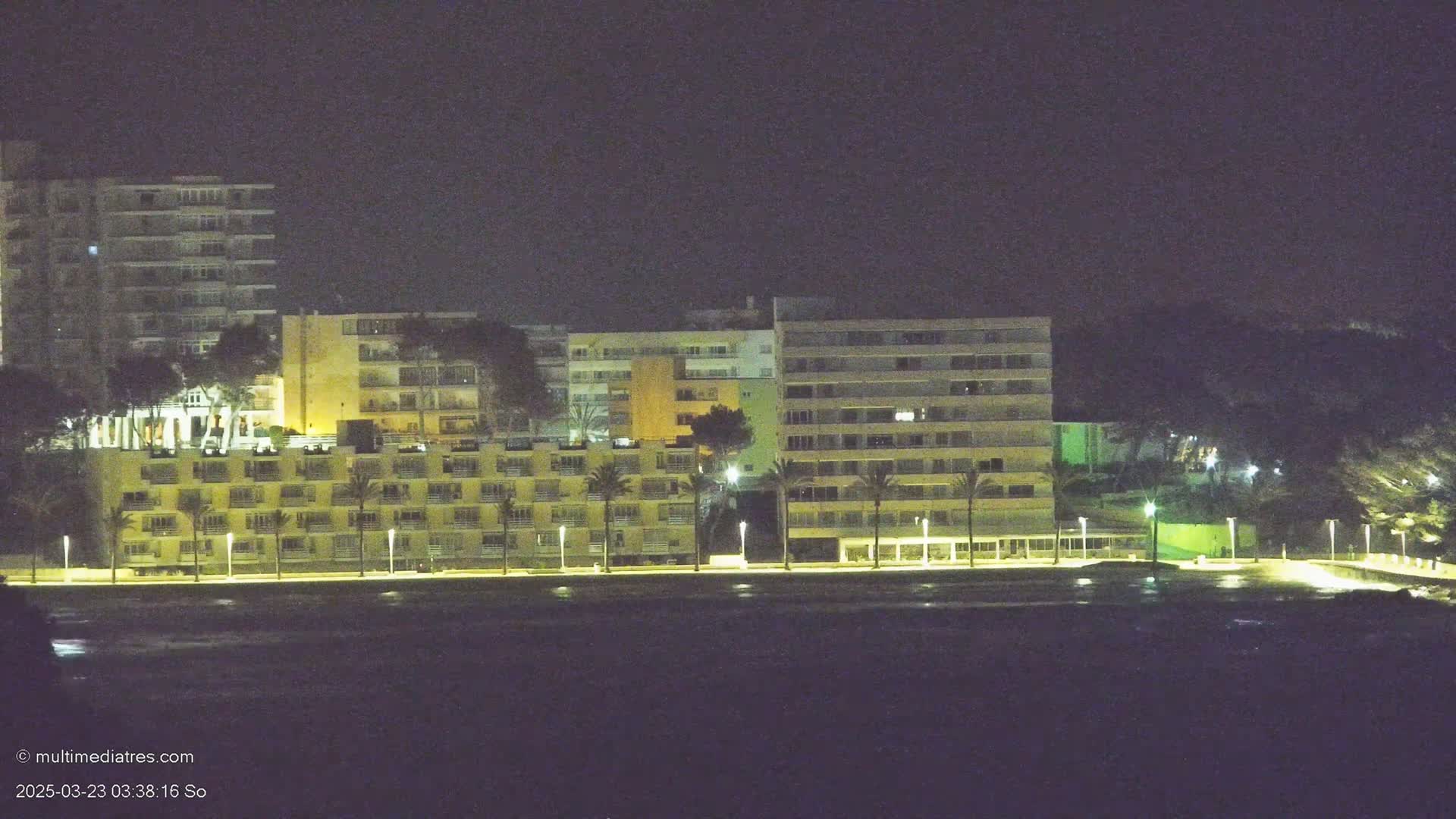 A row of illuminated buildings lines a dark waterfront at night.