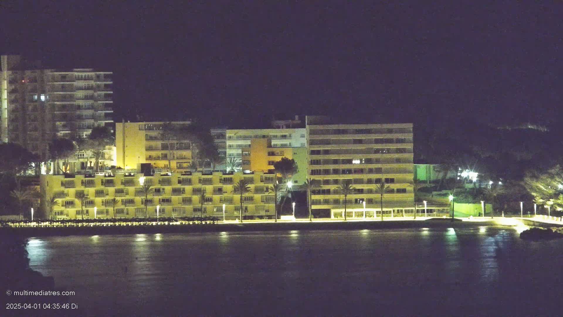 Lit-up hotel buildings line a calm, dark waterfront at night.