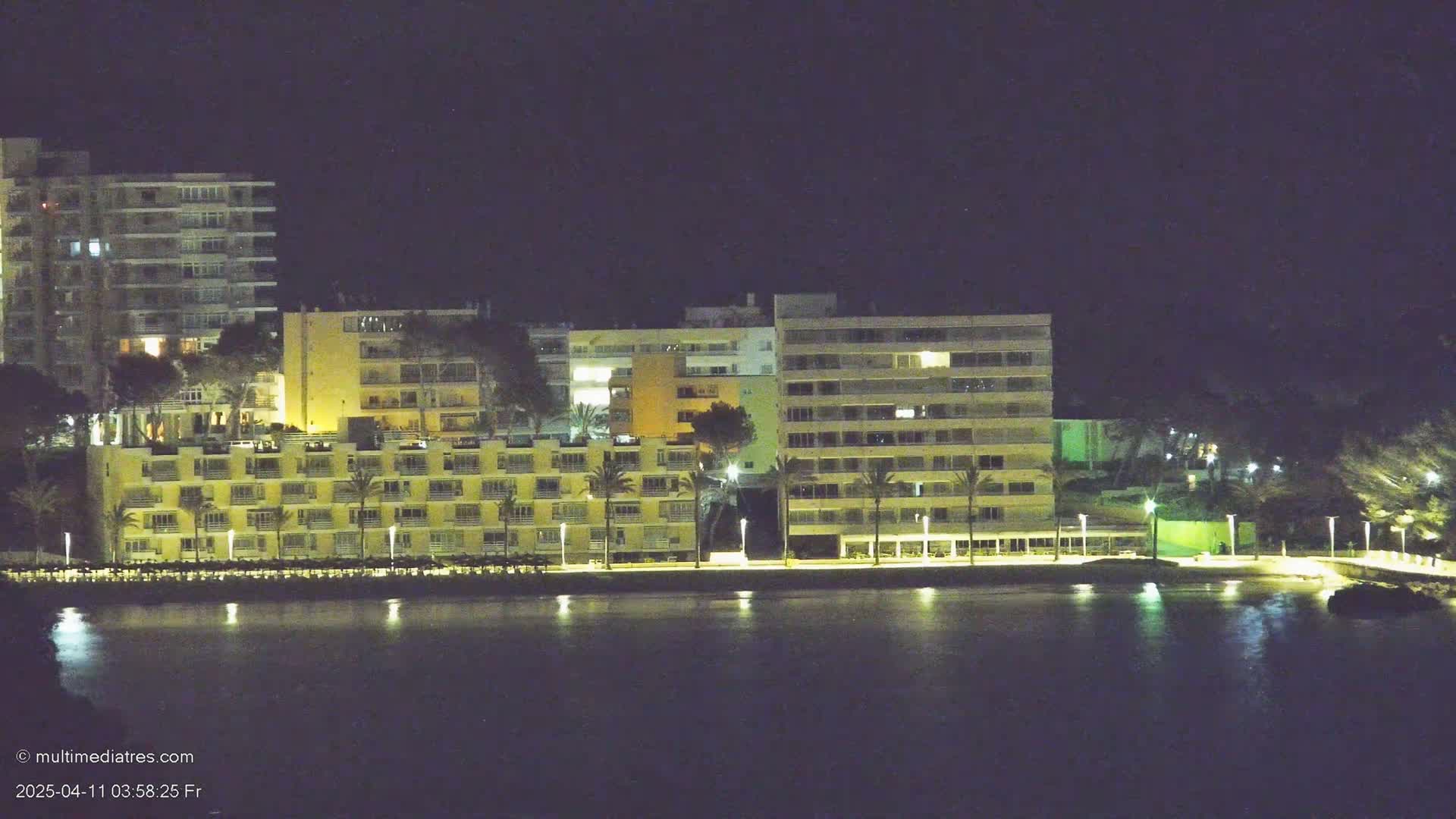 A line of illuminated beachfront hotels and buildings sits beside a dark body of water at night.