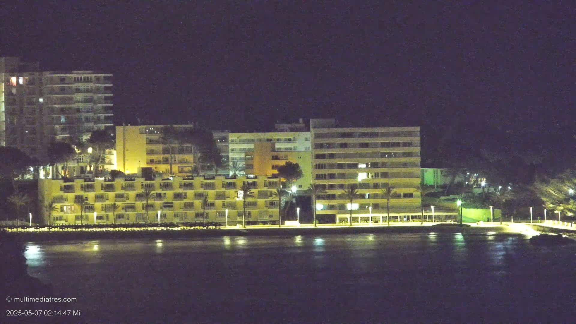 Illuminated multi-story buildings line a waterfront at night.