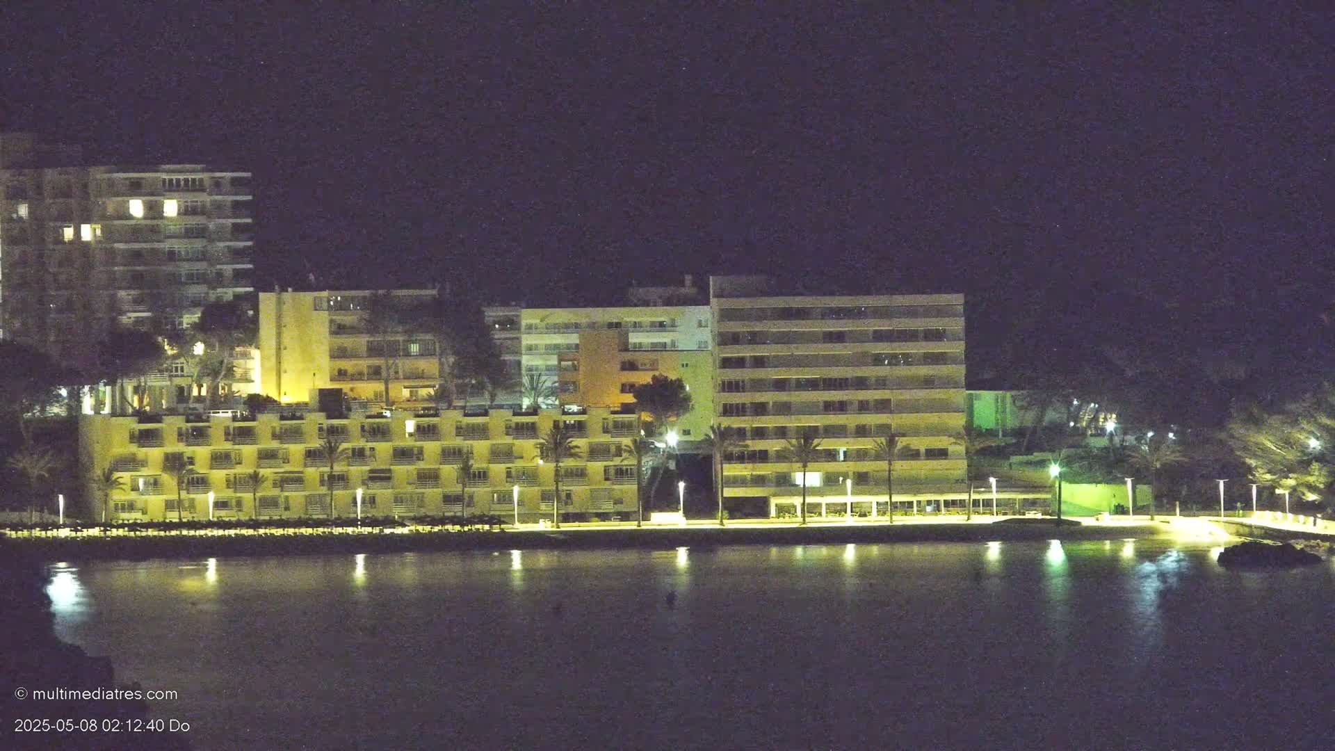 Illuminated multi-story buildings line a dark waterfront at night.