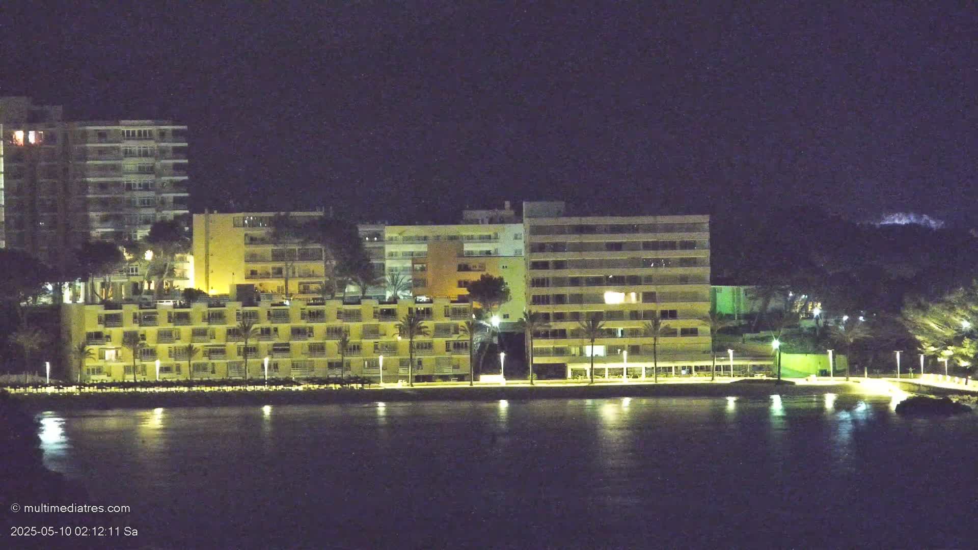 Illuminated multi-story buildings line a dark waterfront at night.