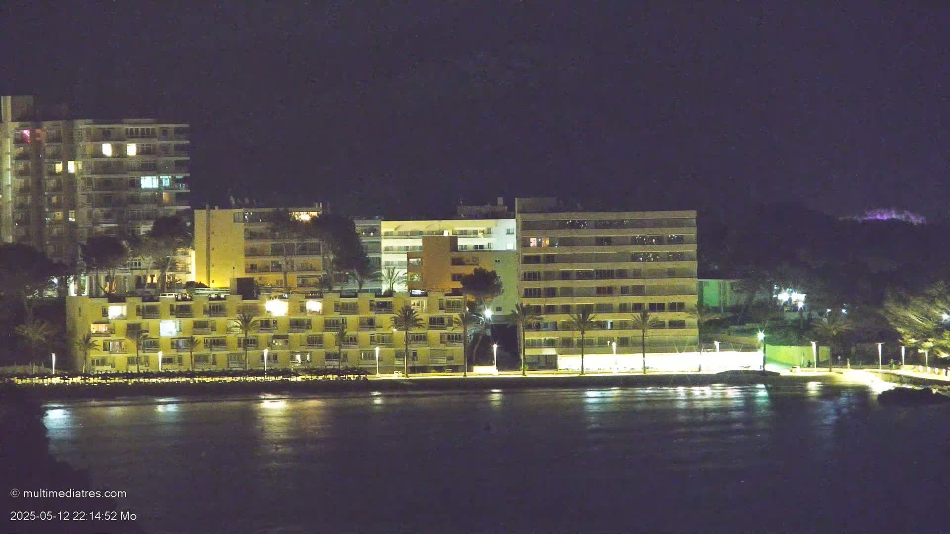 A line of illuminated apartment buildings sits on a waterfront at night.