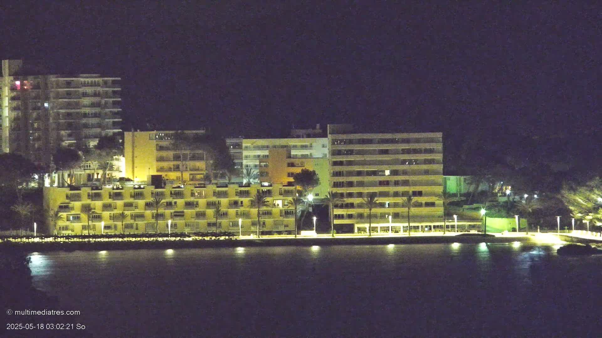 Illuminated multi-story buildings line a waterfront at night.