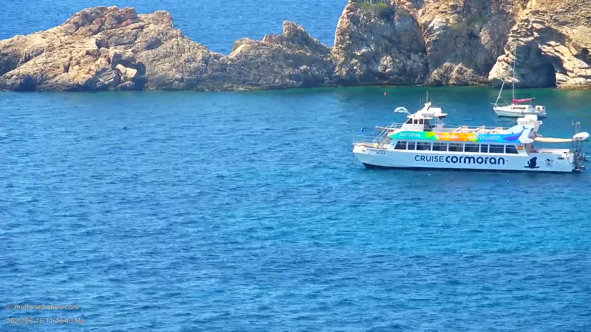A passenger boat is anchored near rocky outcrops in calm blue water.