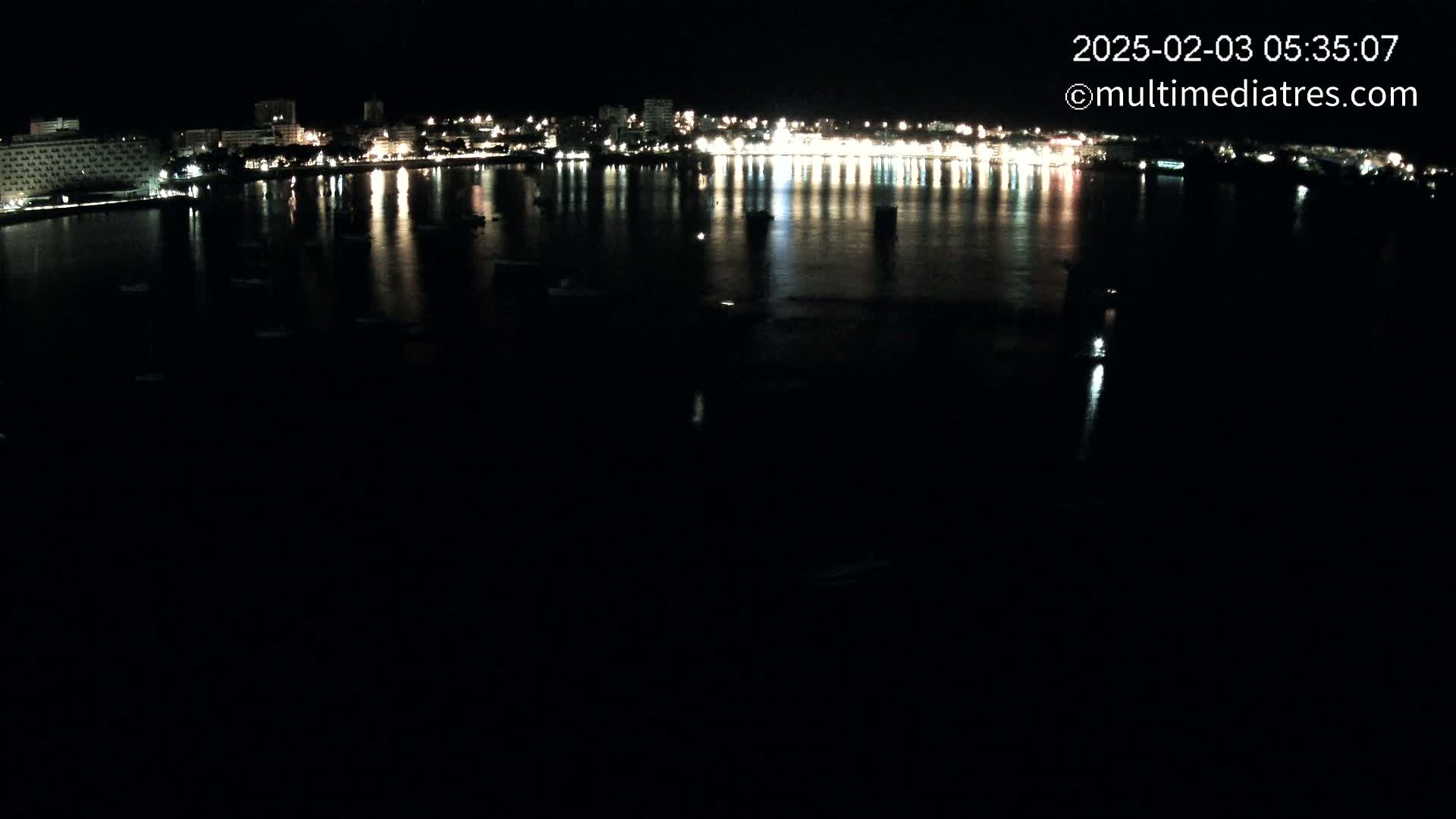 A nighttime view of a calm body of water reflecting the lights of a city skyline across its surface.
