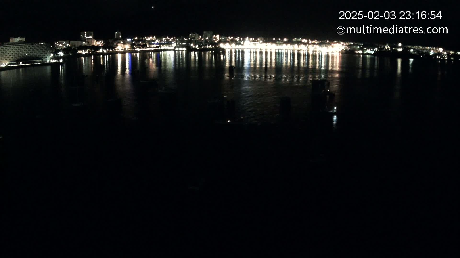 A nighttime view of a city's waterfront, with its lights reflected on calm water.