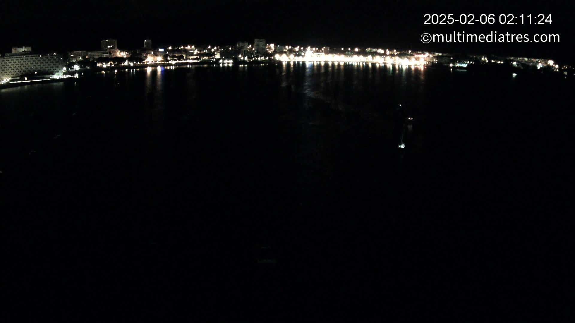 A dark body of water reflects the lights of a city skyline at night.