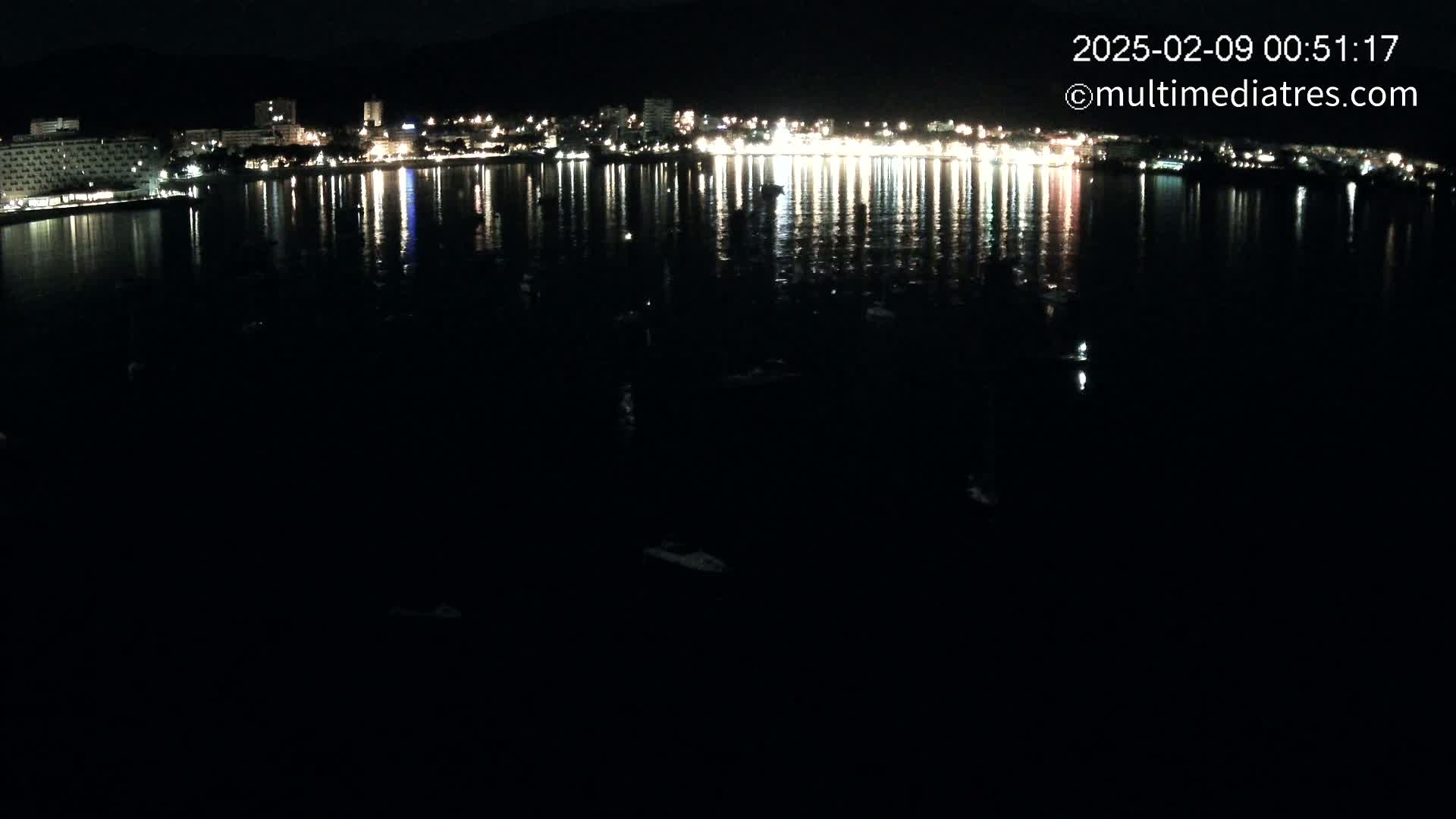 A nighttime view of a city's lights reflected on a calm, dark body of water.
