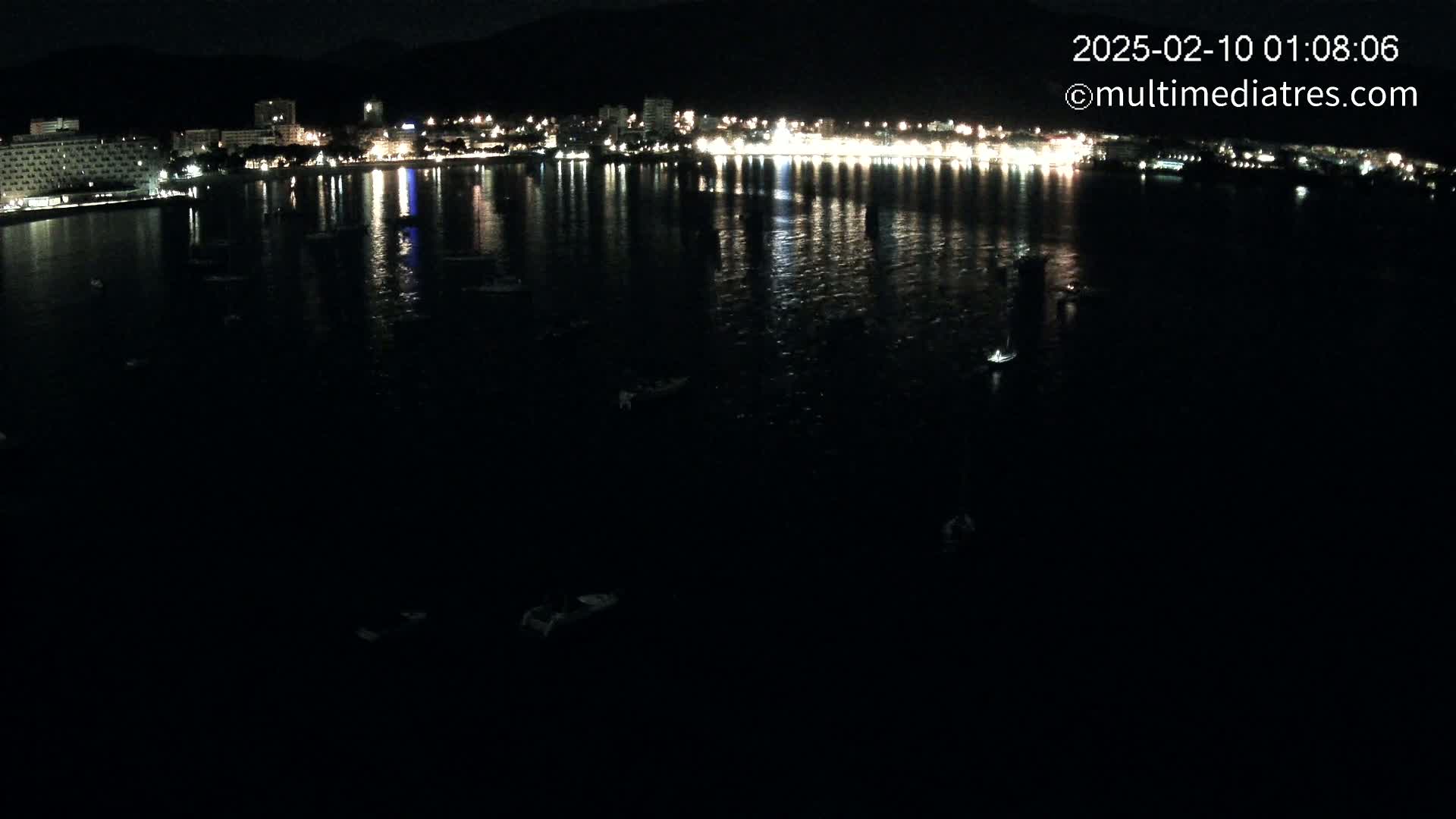A nighttime view of a calm body of water reflecting the lights of a city along a shoreline.