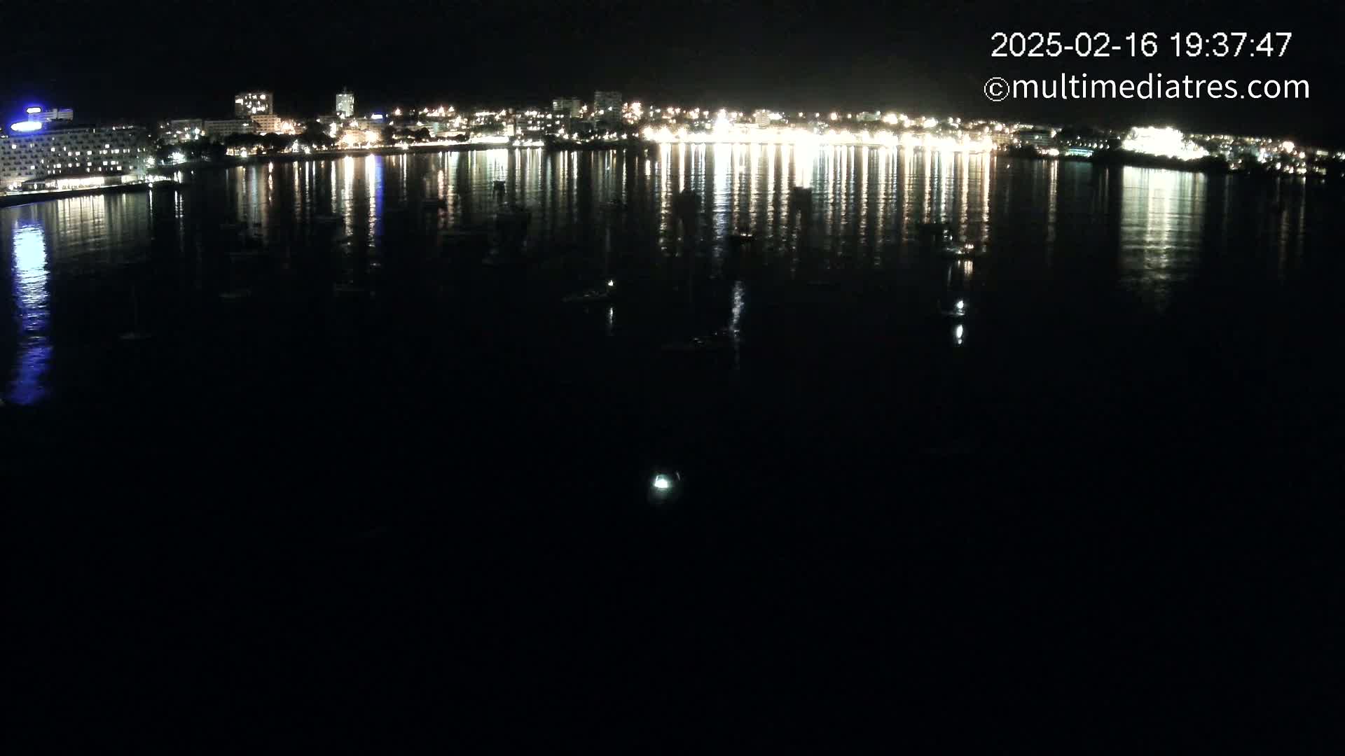 A nighttime view of a city's lights reflected on a calm body of water.