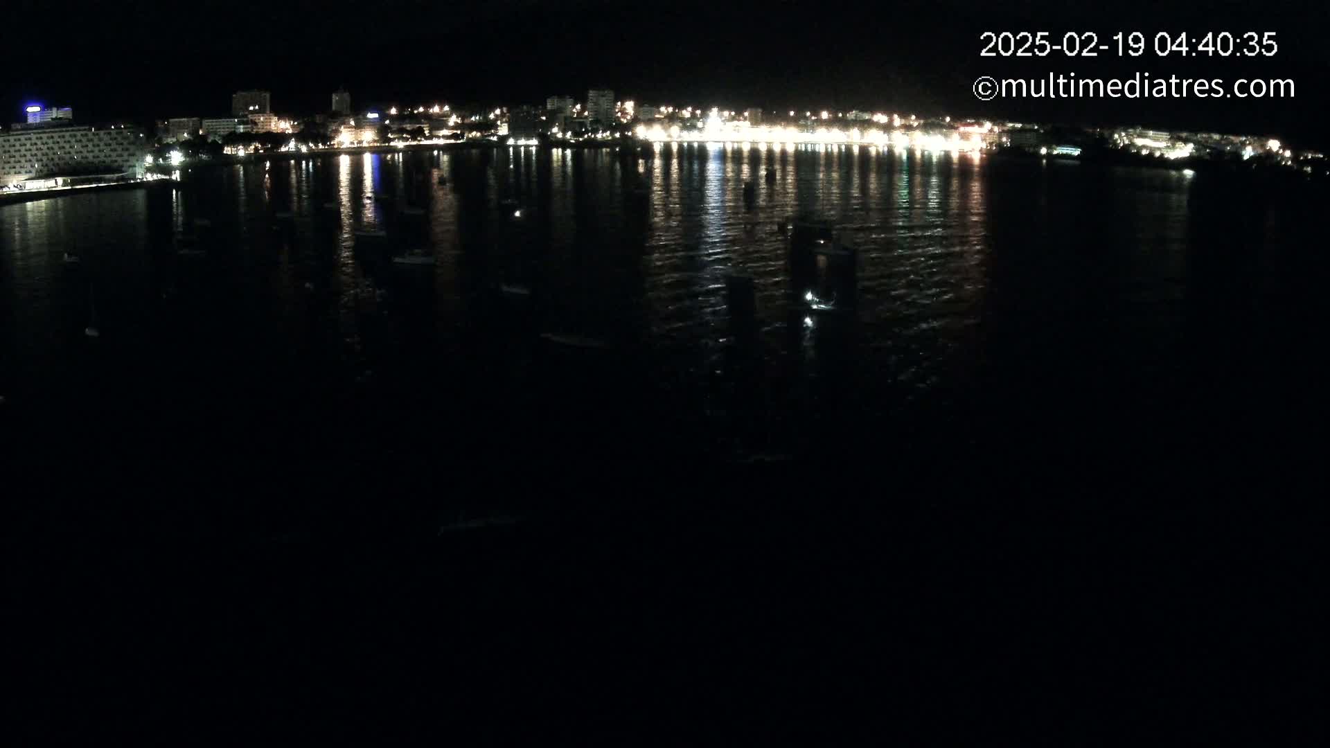 A nighttime view of a calm body of water reflecting the lights of a city skyline.