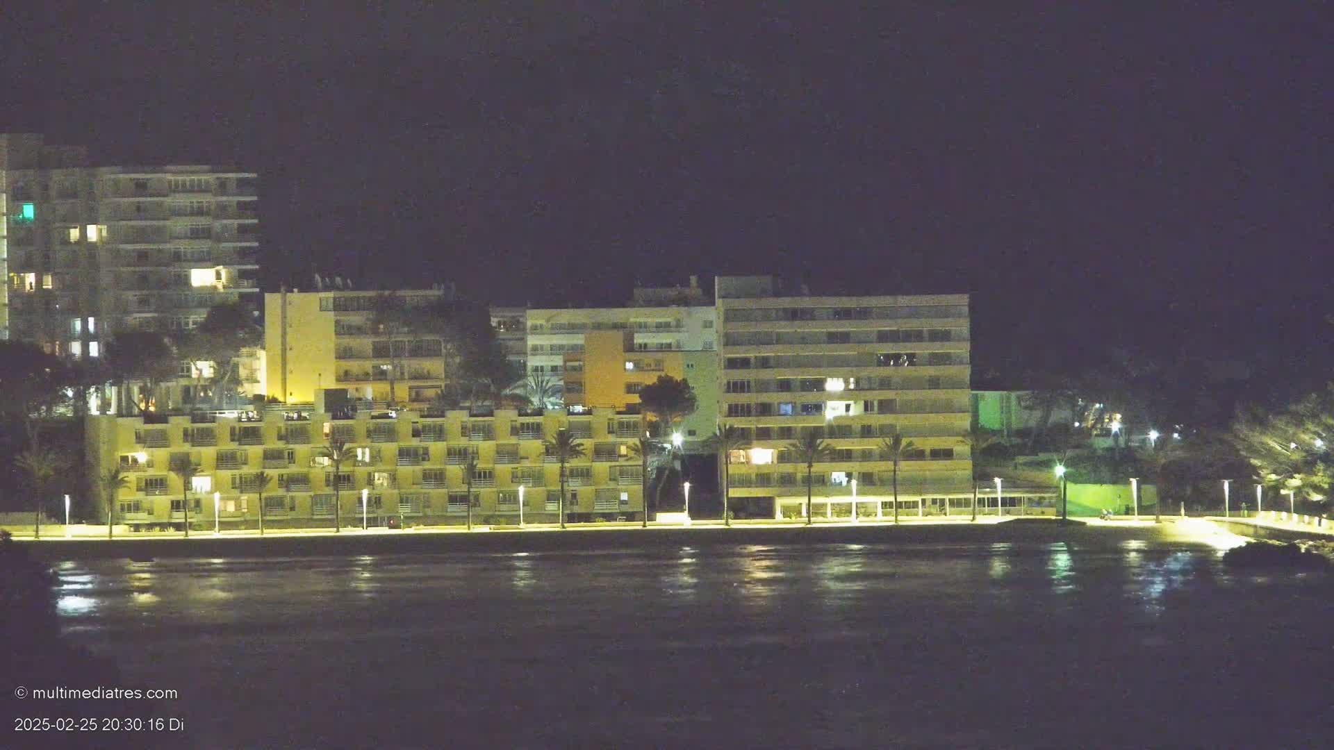 A line of illuminated buildings stands along a dark waterfront at night.