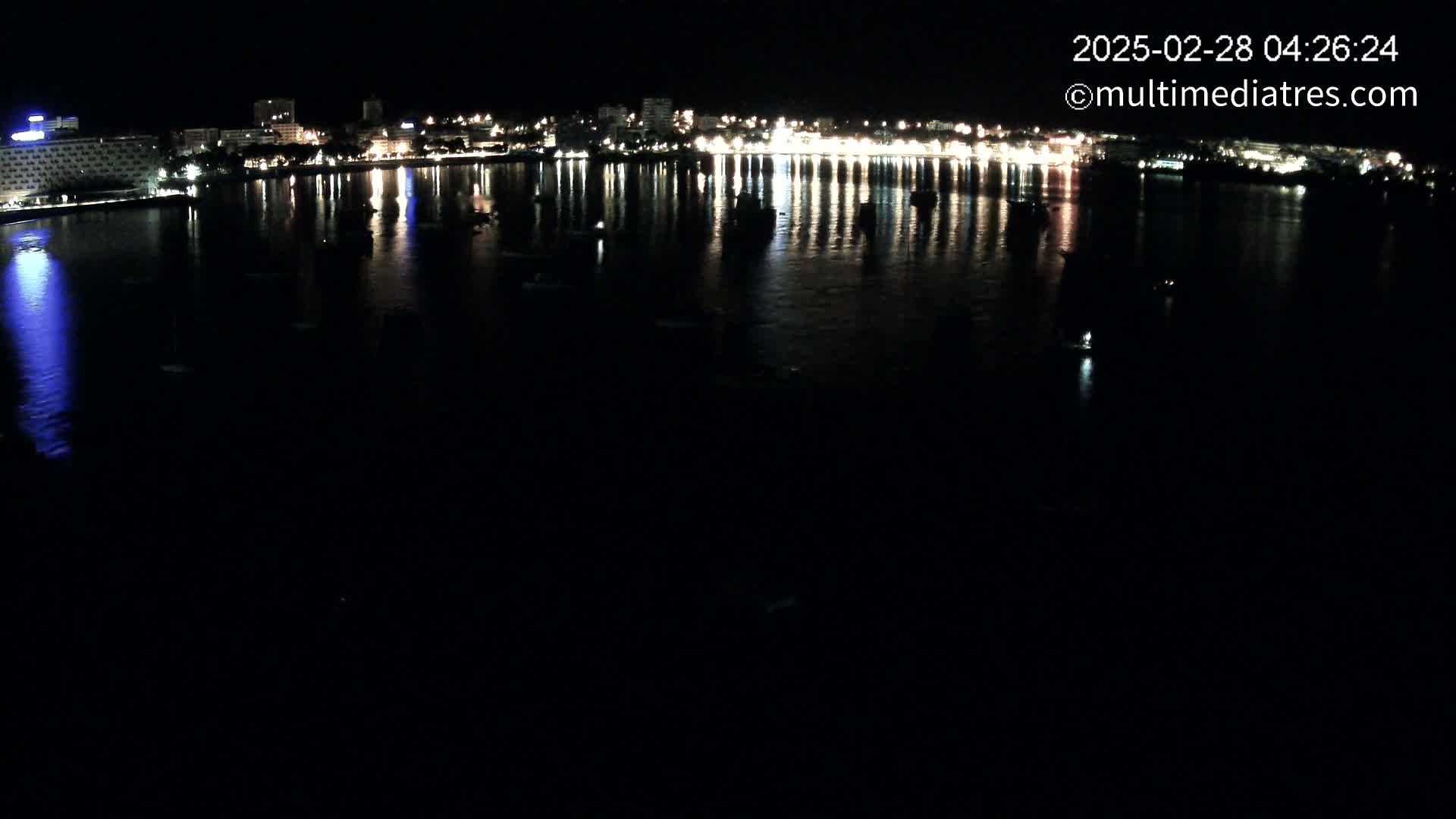 A nighttime view of a calm body of water reflecting the lights of a city skyline.