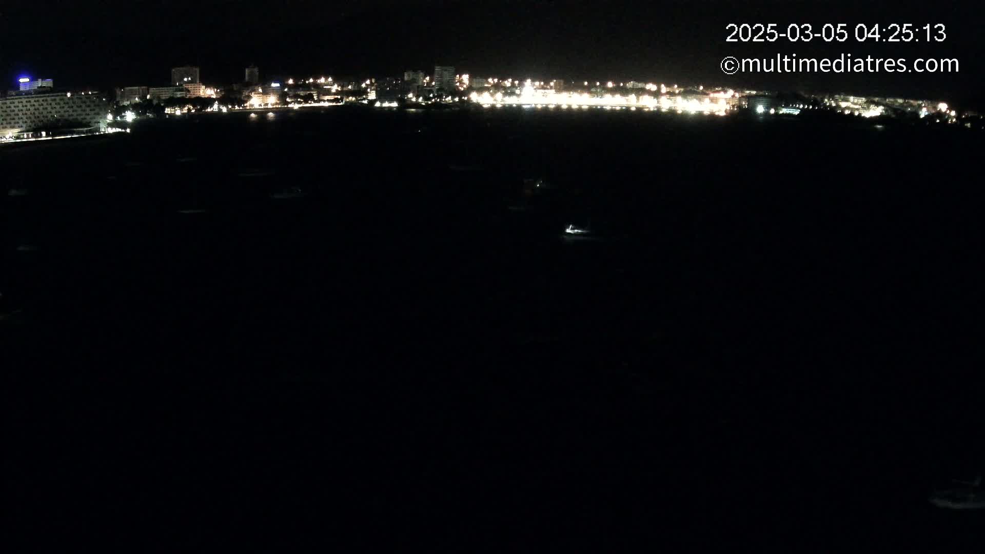 A nighttime view of a dark body of water with a distant, illuminated cityscape on the horizon.