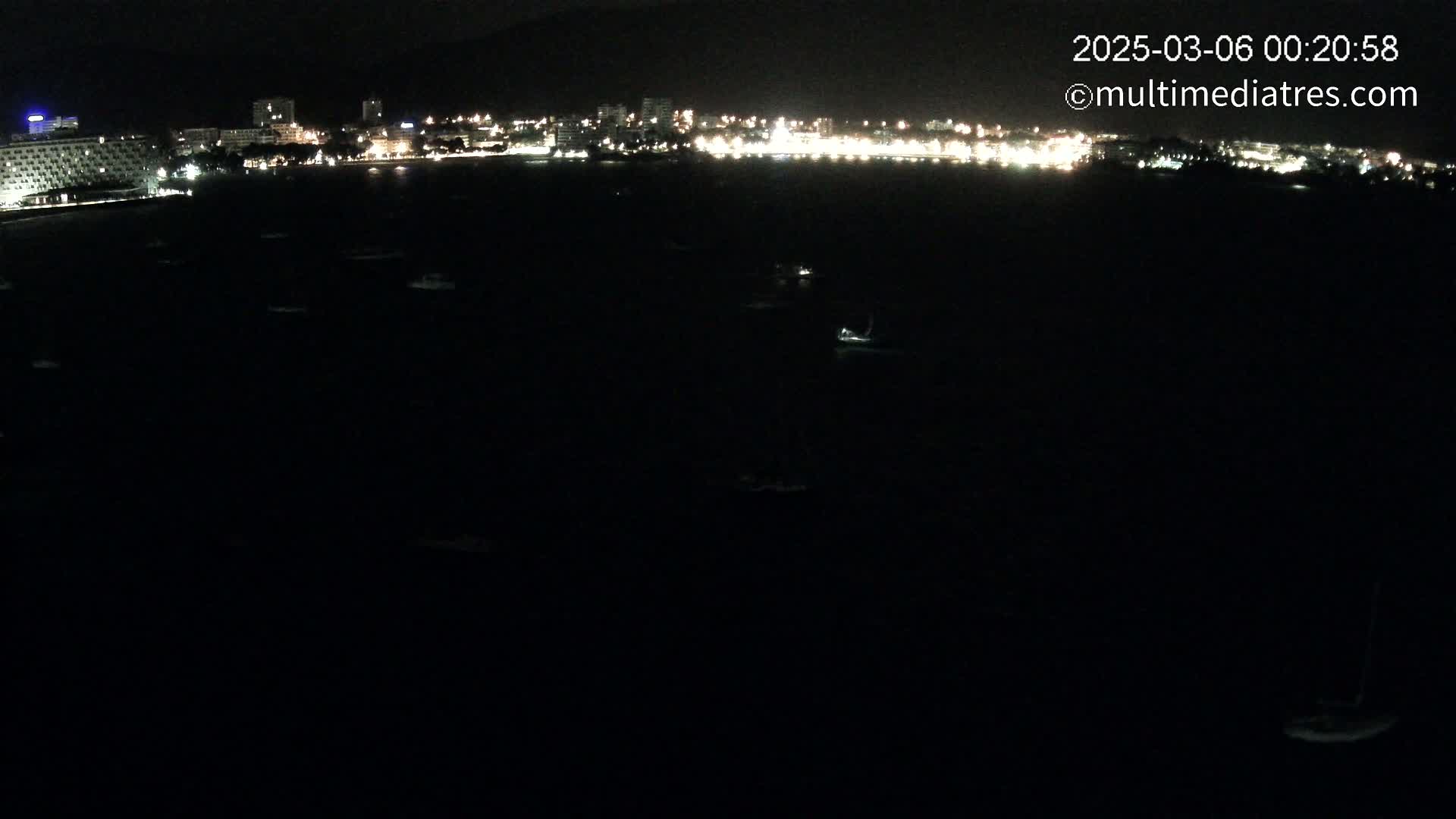A nighttime, dark view of a city skyline across a body of water dotted with small lights.