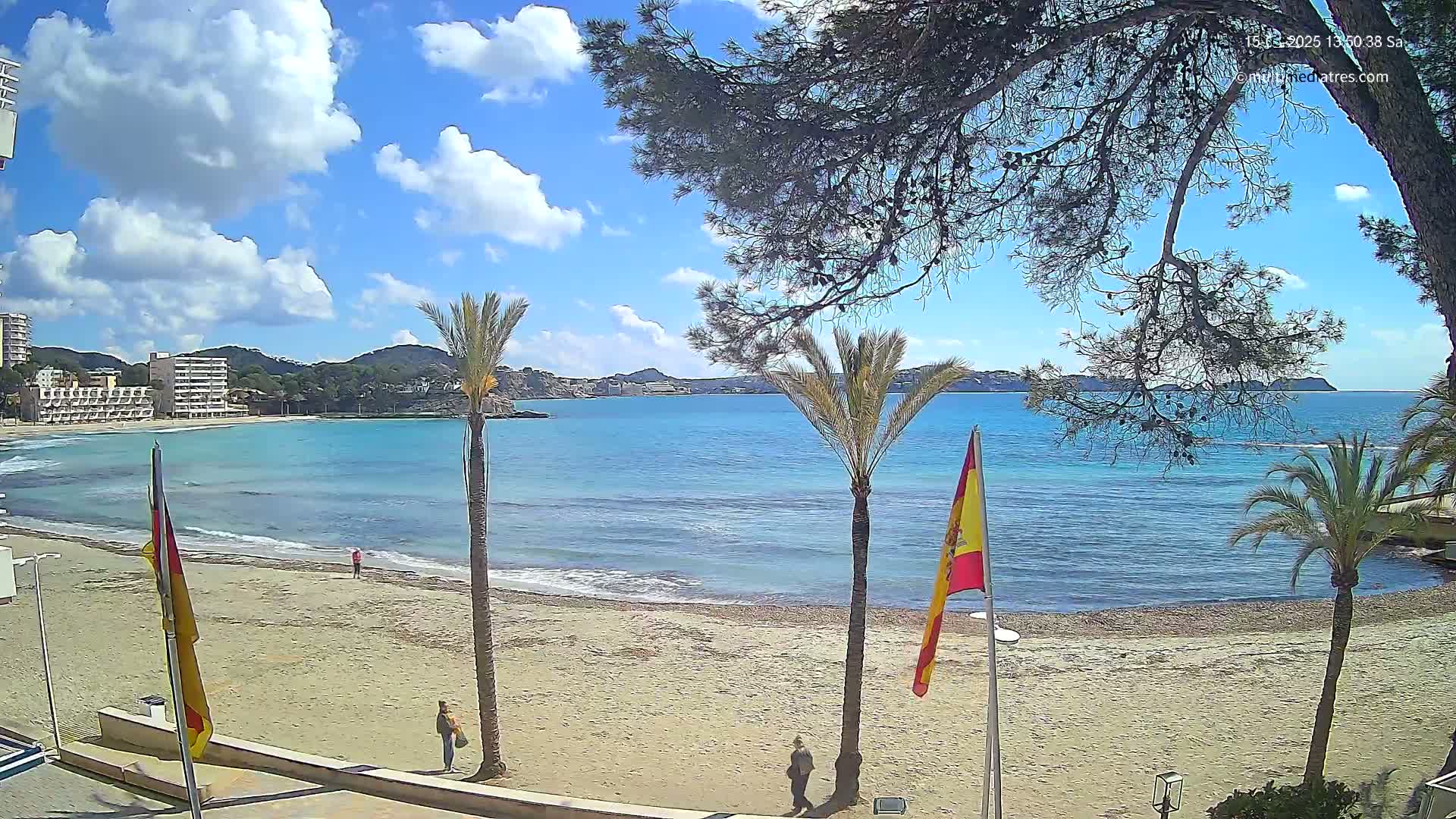 A sandy beach with palm trees and a calm, turquoise sea under a partly cloudy blue sky.