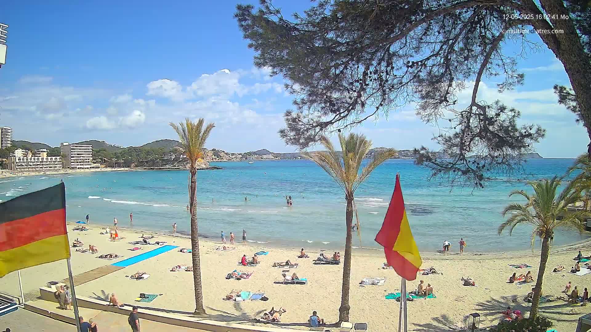 A sunny day at a sandy beach with clear turquoise water, palm trees, and people relaxing on the shore.