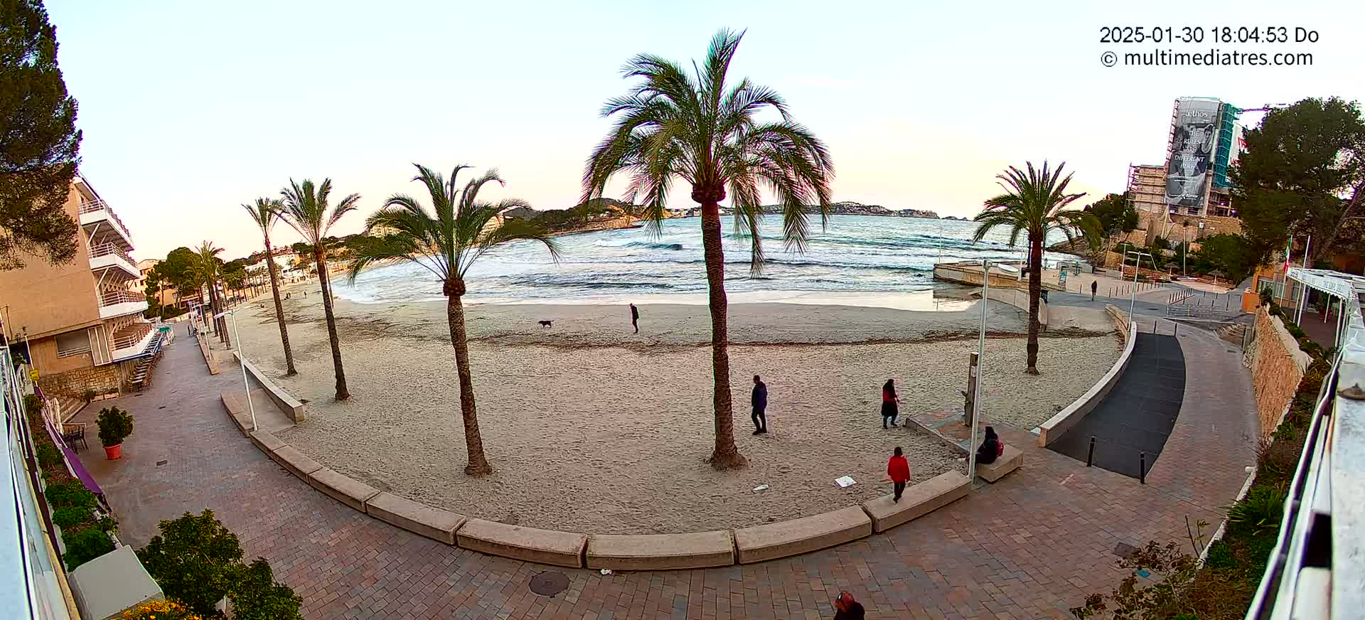 A sandy beach with palm trees and several people is visible, with slightly wavy ocean water under a clear, dusky sky.