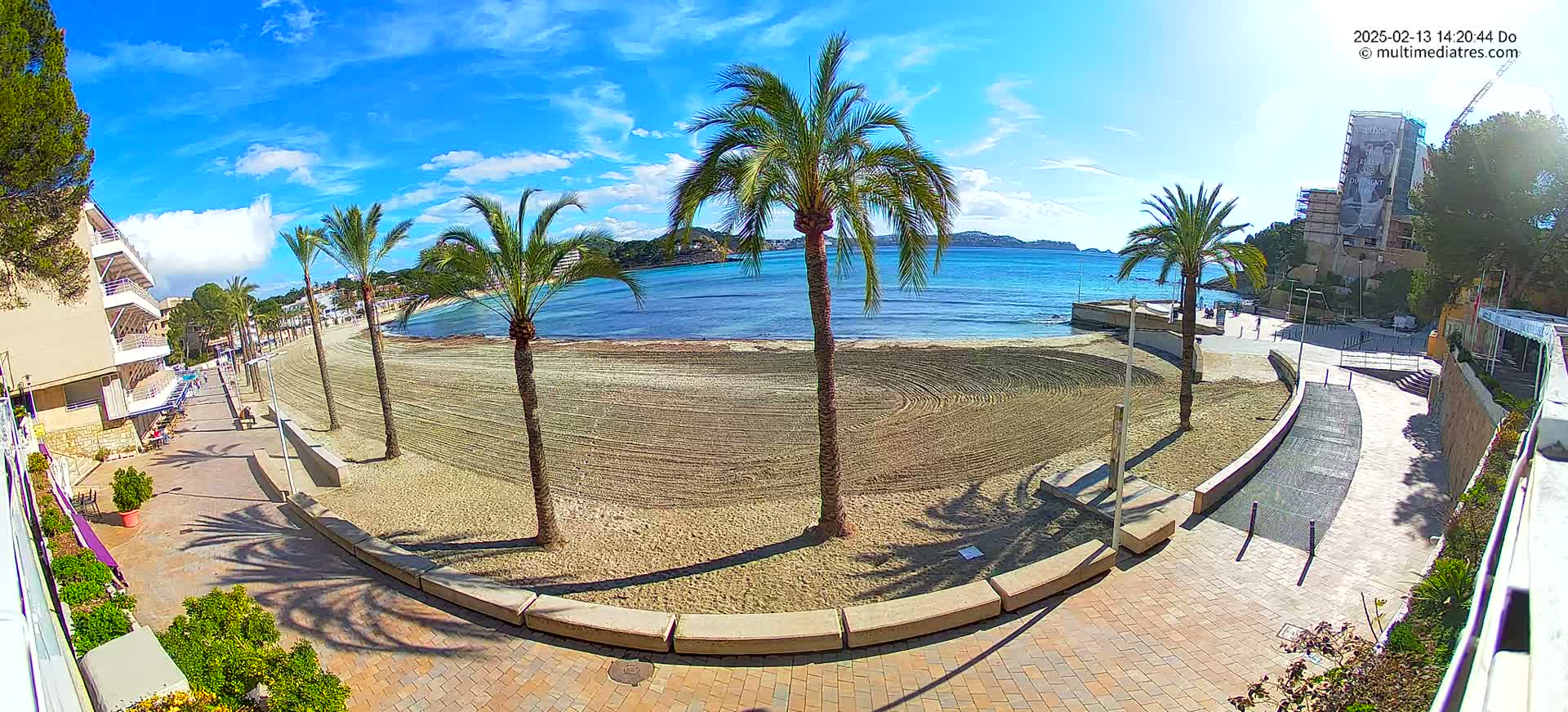A sandy beach with palm trees and buildings is visible under a mostly sunny sky.