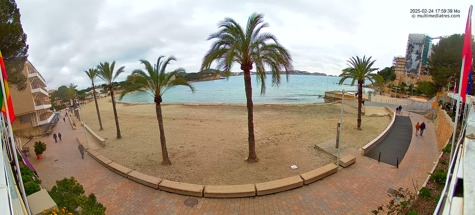A sandy beach with palm trees is visible, overlooking a calm bay under an overcast sky.