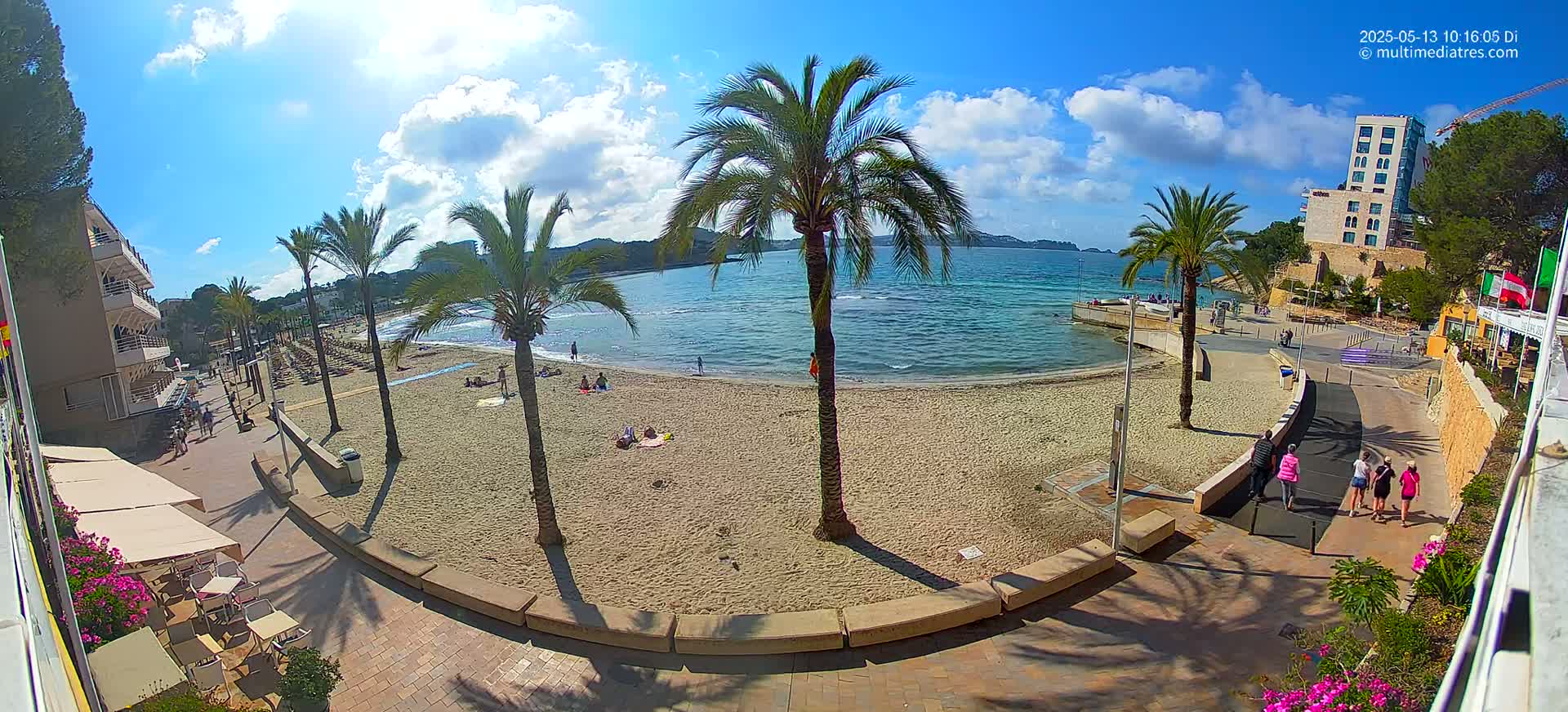 A sandy beach with palm trees and several people on a sunny day with some clouds in the sky.