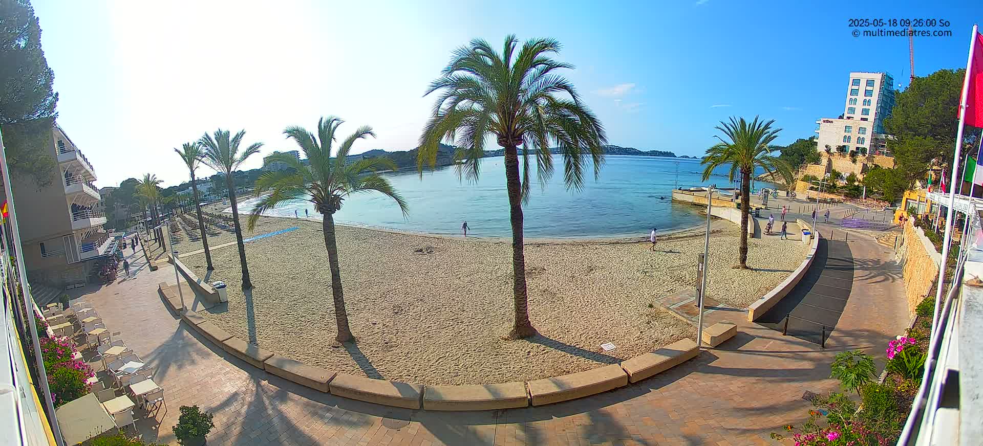 A sandy beach with palm trees and a few people is visible, overlooking calm, blue water under a sunny sky.